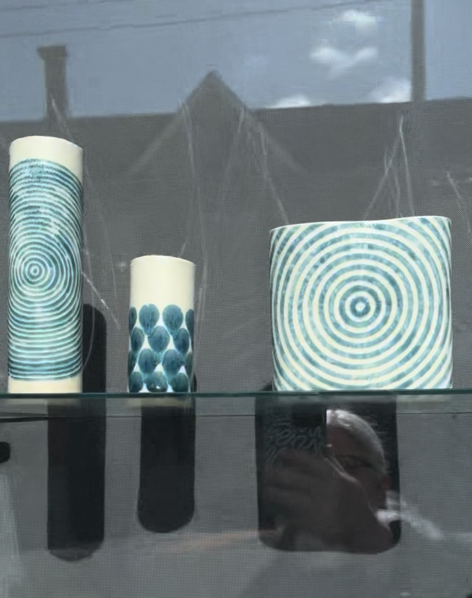 Decorative glass vases with blue spiral and dot patterns on a glass shelf, reflected in the surface below.