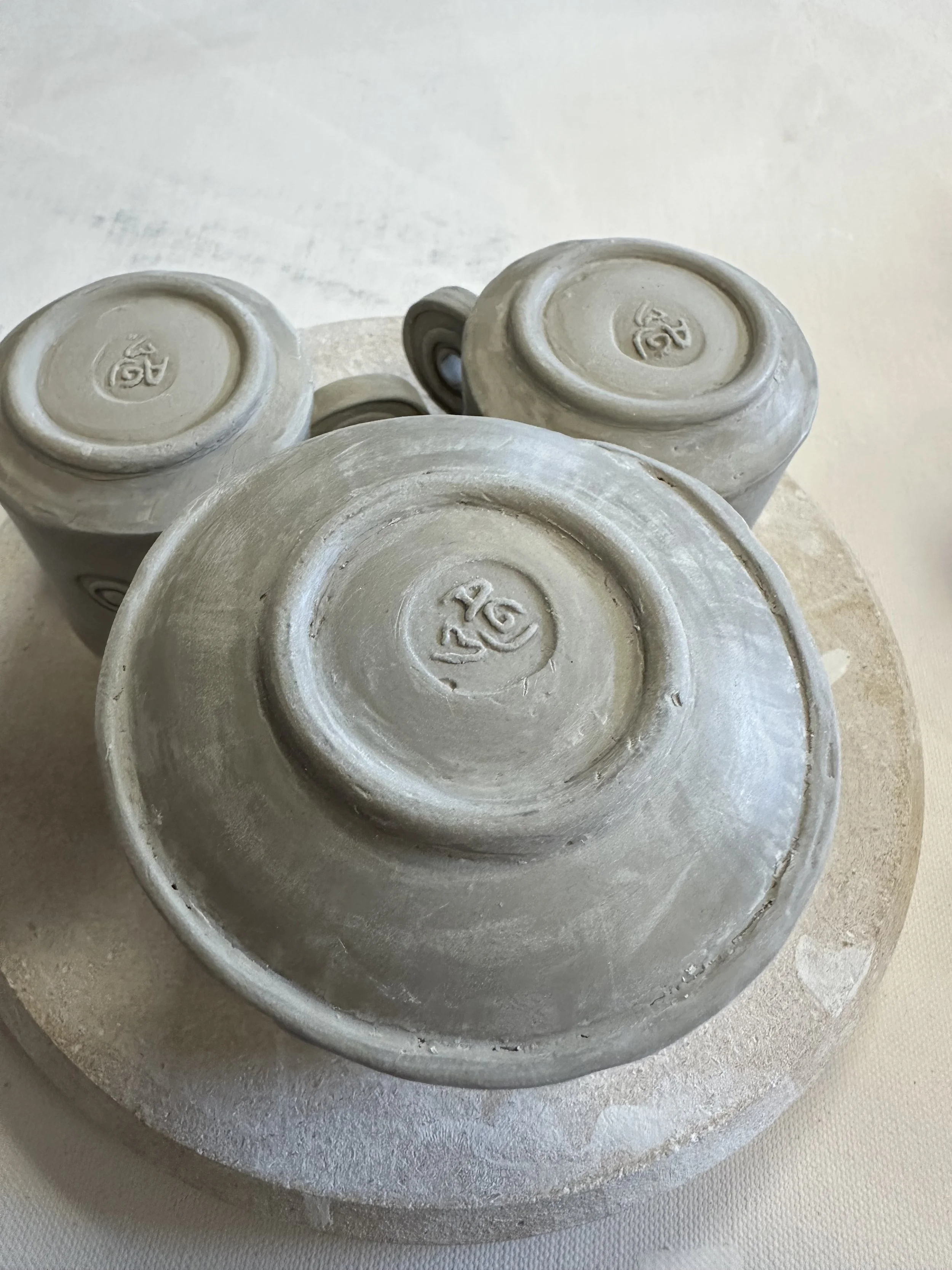 Bottom view of three ceramic cups with stamped markings, placed on a round base.