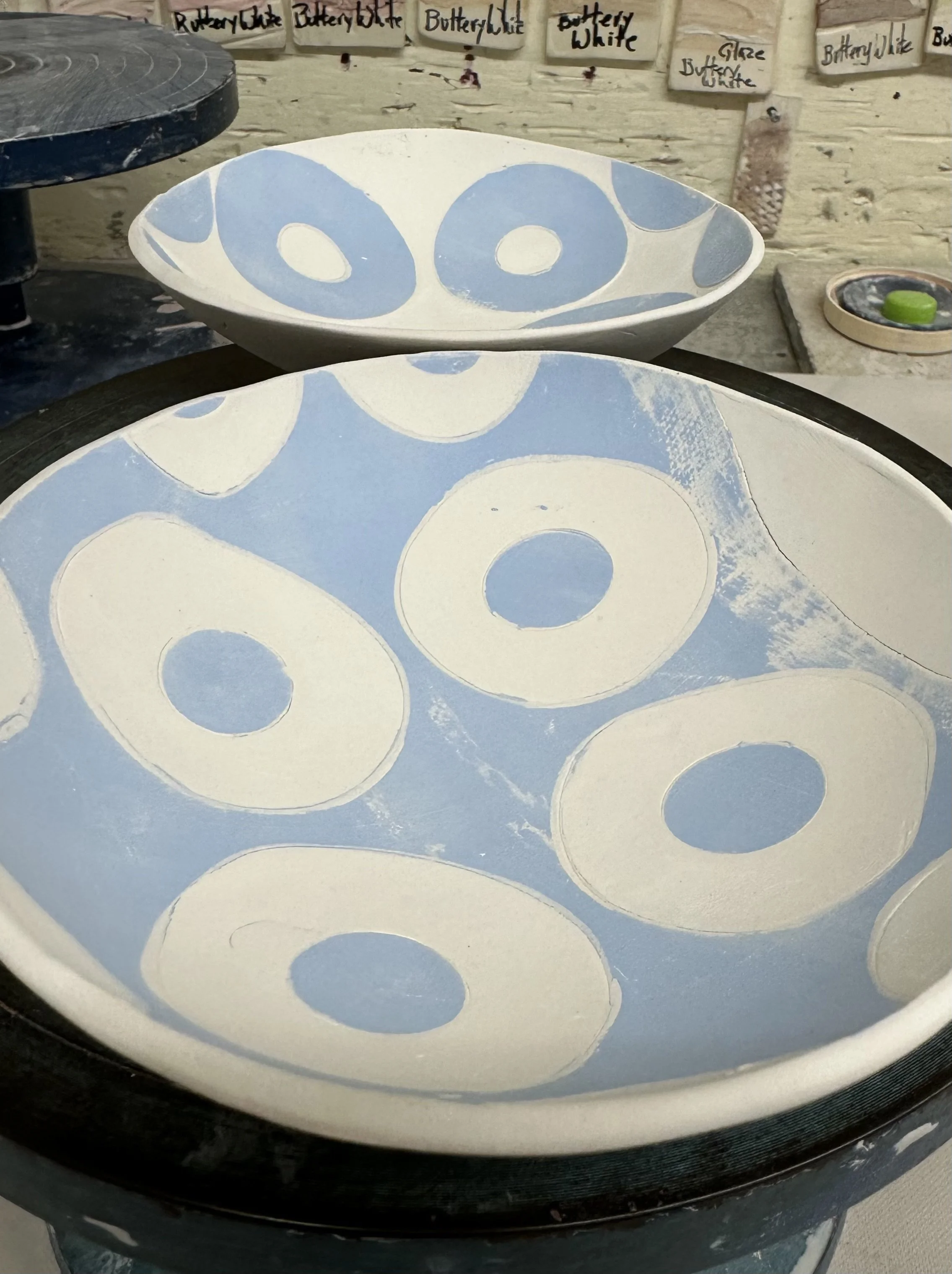 Two ceramic bowls with blue and white circular patterns, placed on a wooden surface, with labels on the wall behind them indicating that the bowls are for butter white.
