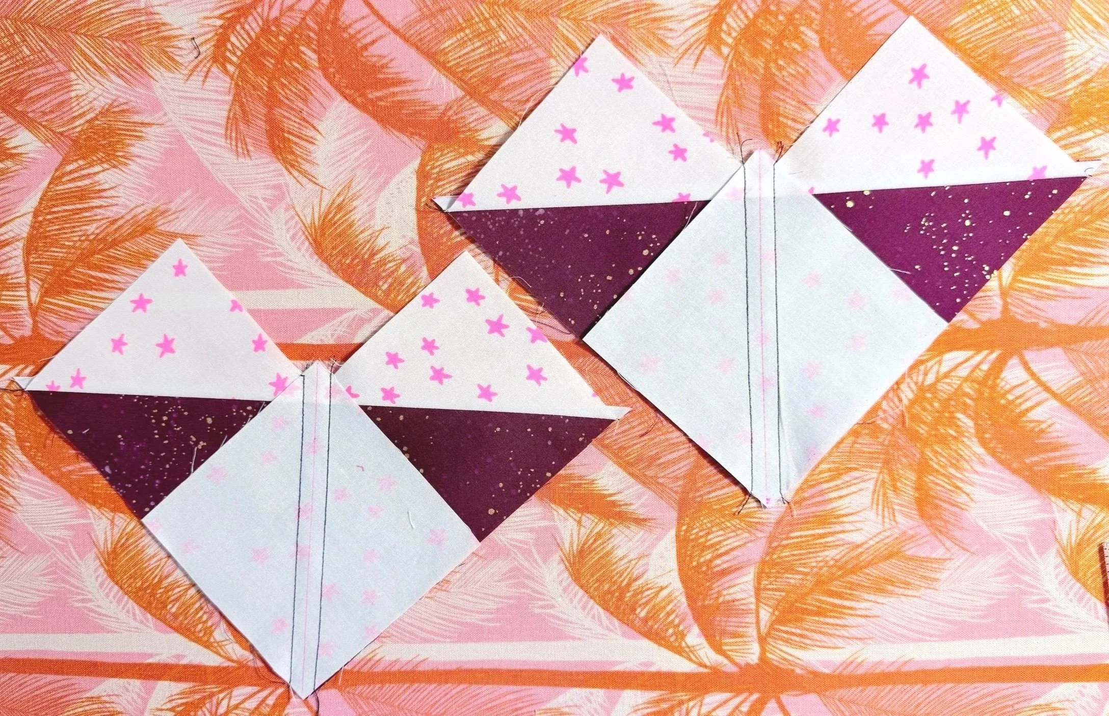2 partially finished quilt blocks consisting of heart shaped units with a square of white fabric sewn facing down, lined up with the bottom corner of the heart shape. A vertical line bisects the square diagonally. Black stitches on both sides of line