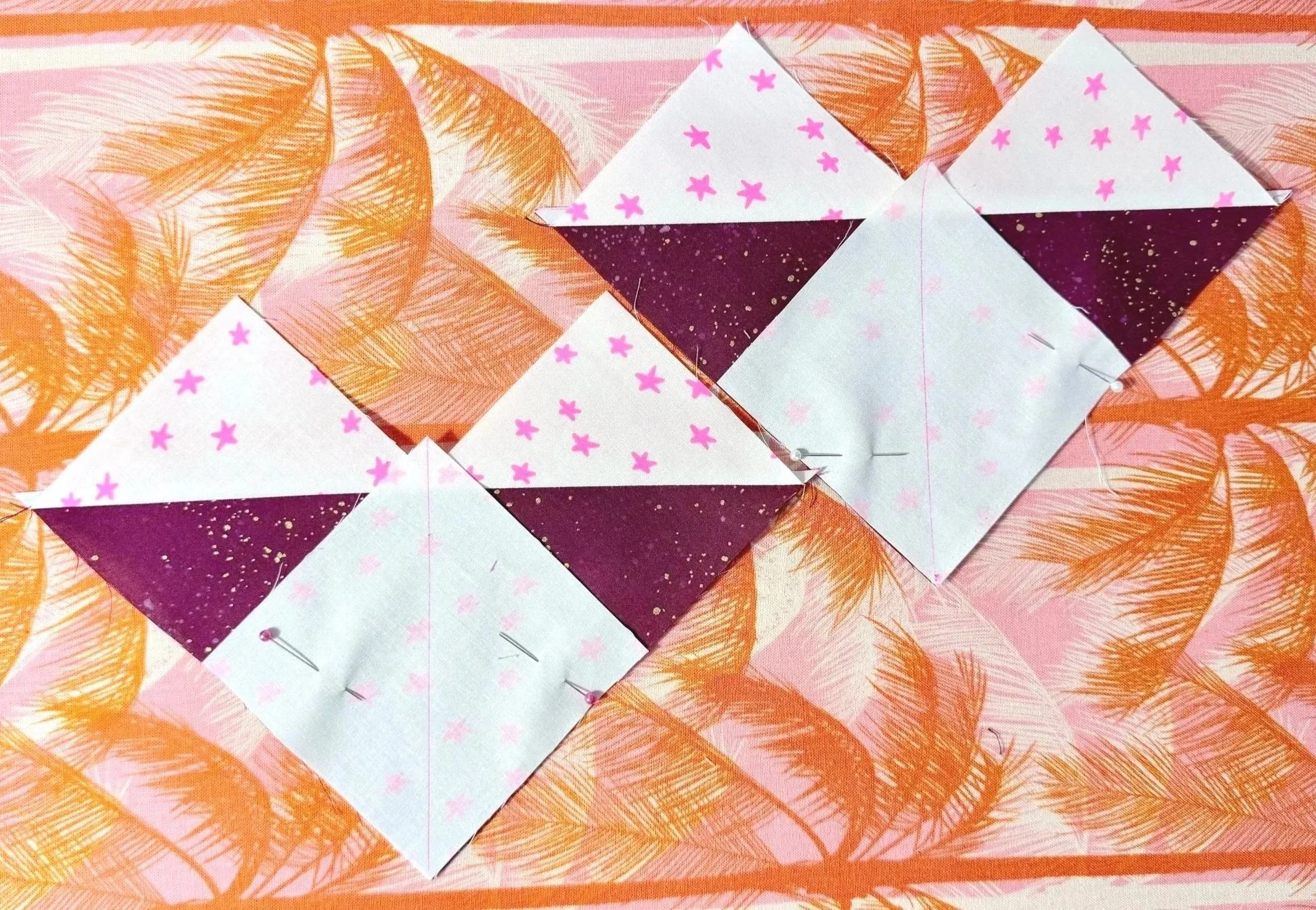 2 partially finished quilt blocks consisting of heart shaped units with a square of white fabric pinned facing down, lined up with the bottom corner of the heart shape. A vertical line bisects the square diagonally.