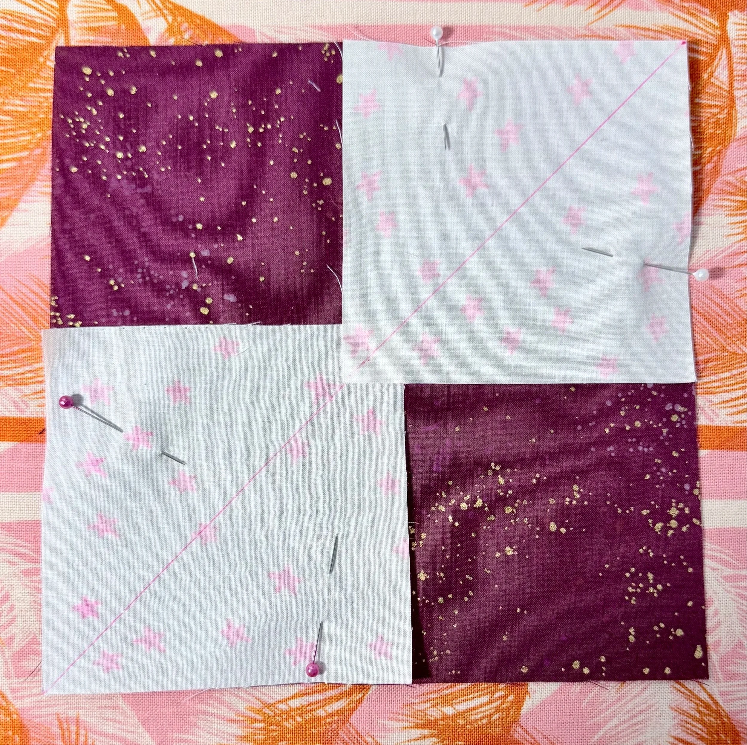 a sparkly maroon square piece of fabric with 2 overlapping pieces of white fabric with neon pink stars, placed upside down on opposite corners of the larger square. 4 pins secure the small squares of fabric.