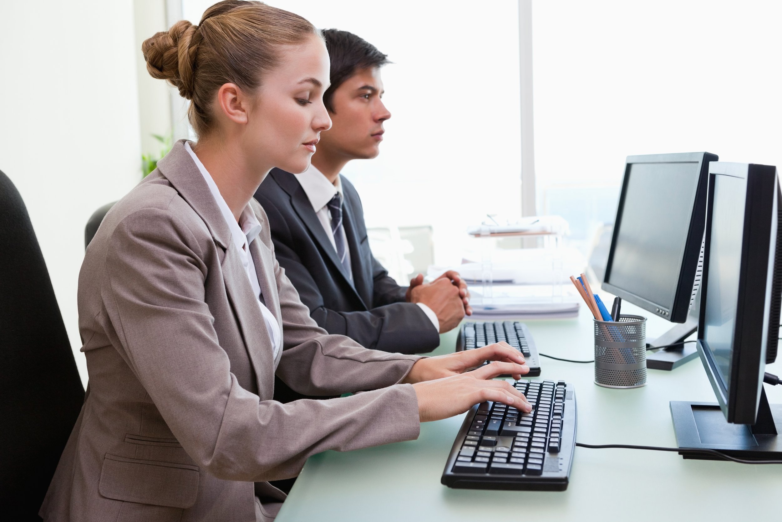 Two professionals, a woman and a man, working at computers in an office.