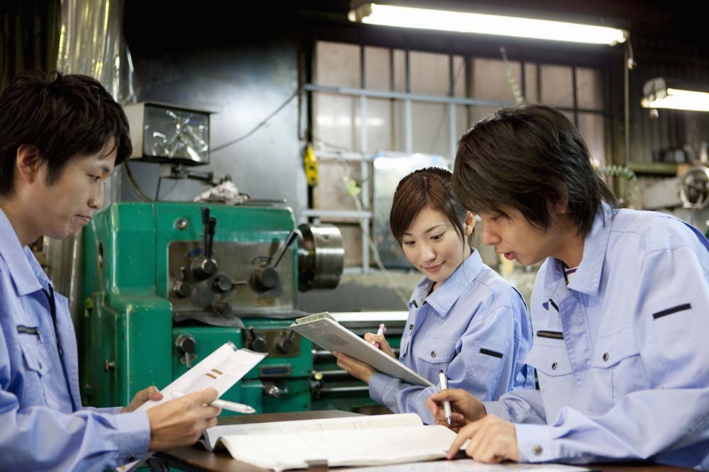 Four people in blue uniforms studying documents in a workshop with machinery.