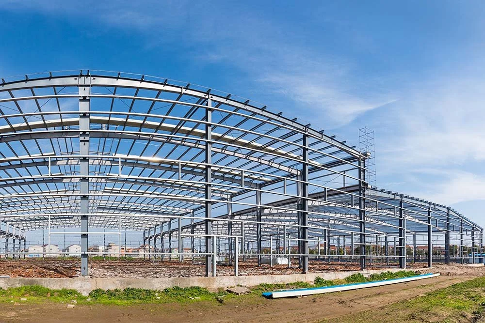 Steel framework of a large greenhouse under construction with a clear blue sky