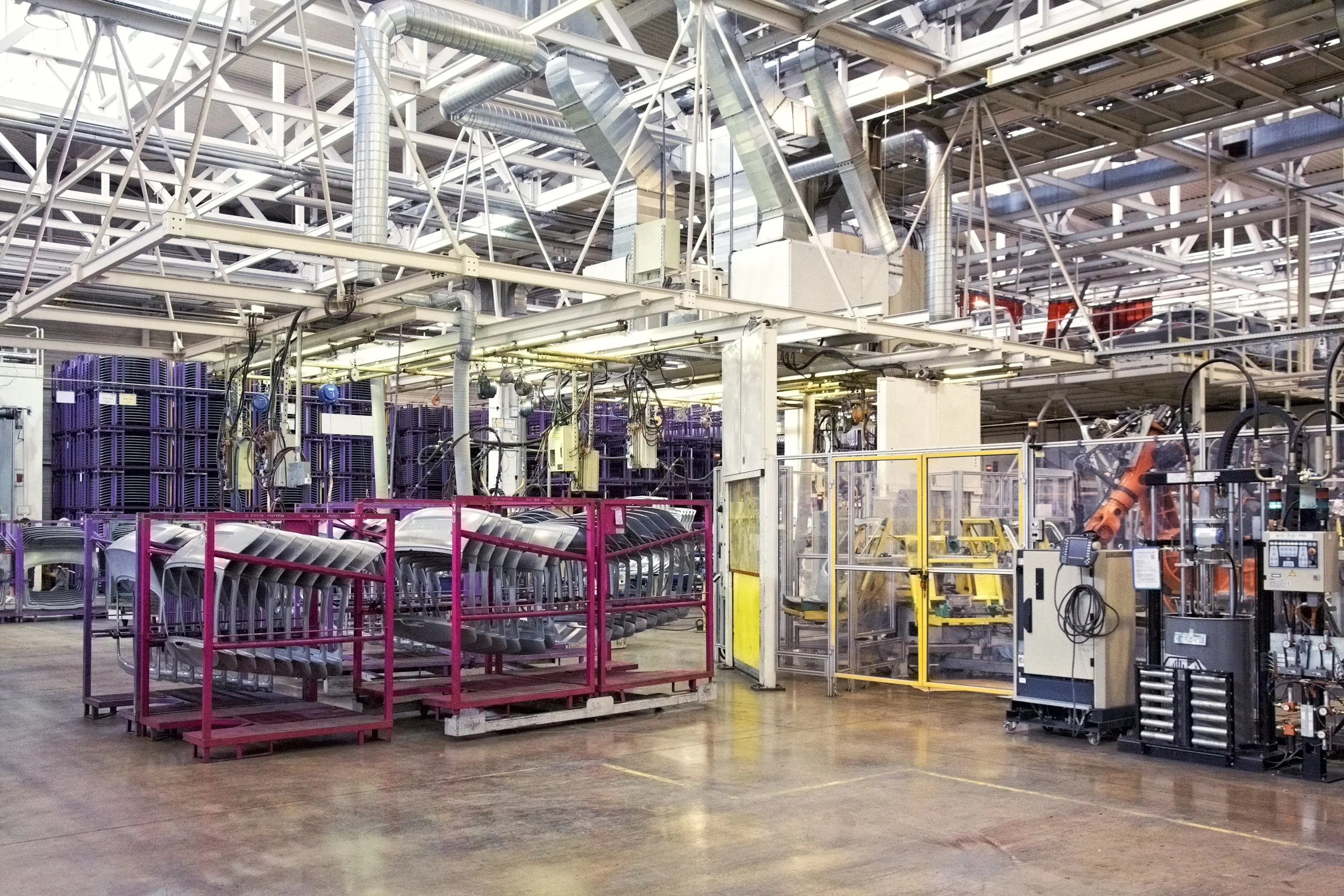 An industrial manufacturing facility with machinery, metal frames, and conveyor systems, inside a large warehouse.