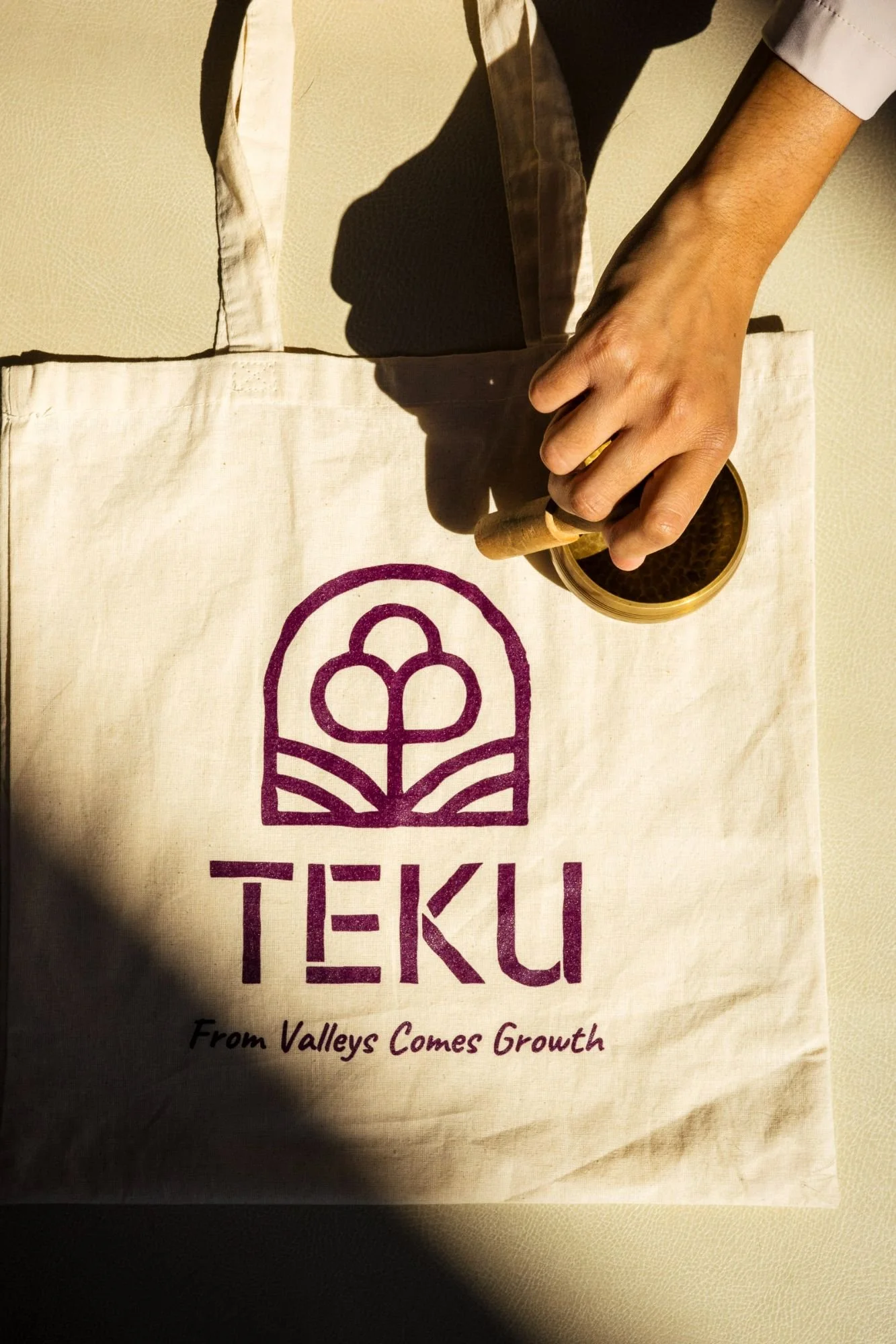 A person using a stamp on a canvas bag with the TEKU logo and the slogan "From Valleys Comes Growth."