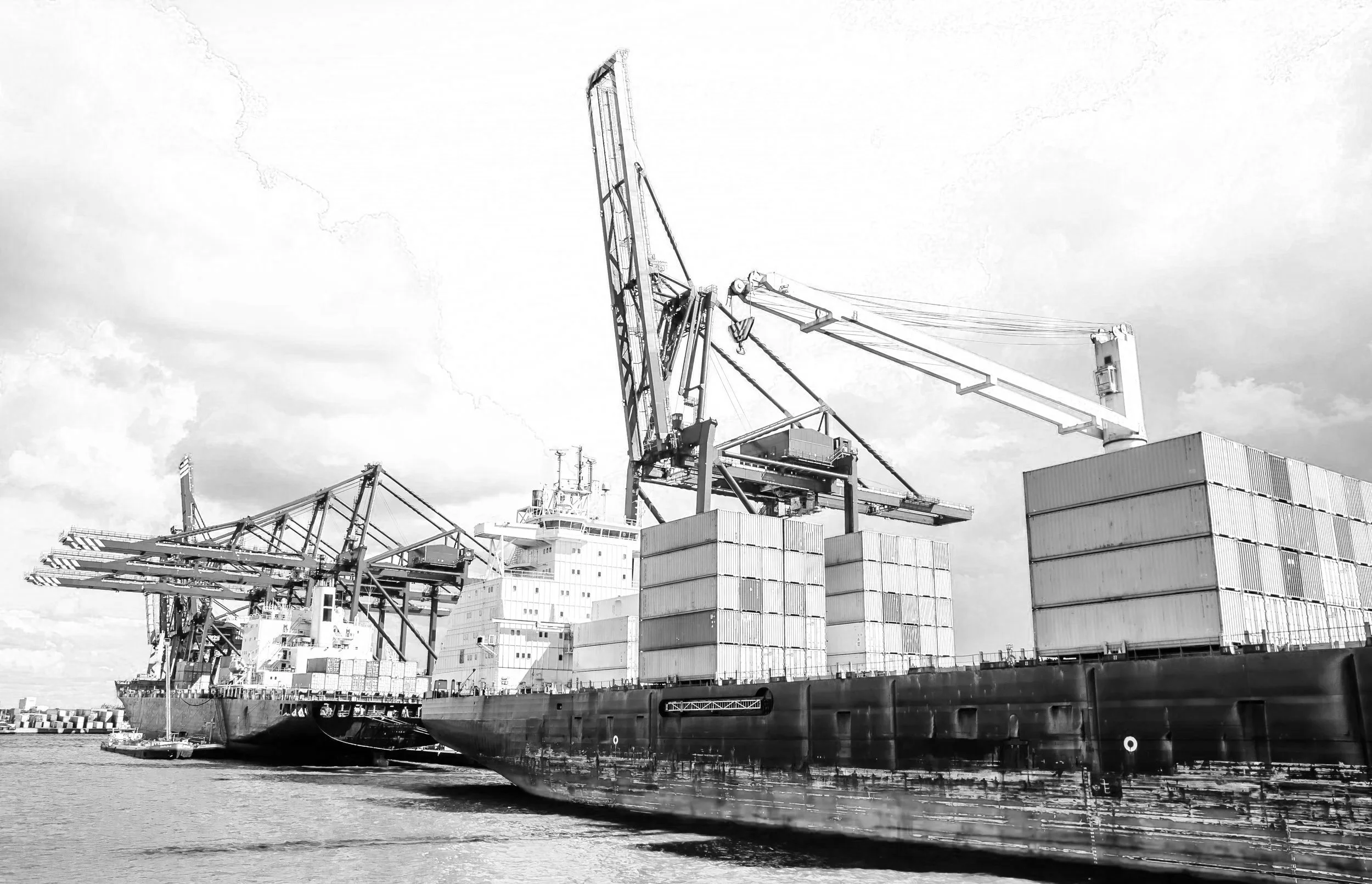 Large cargo ship docked at port with containers and cranes in black and white.