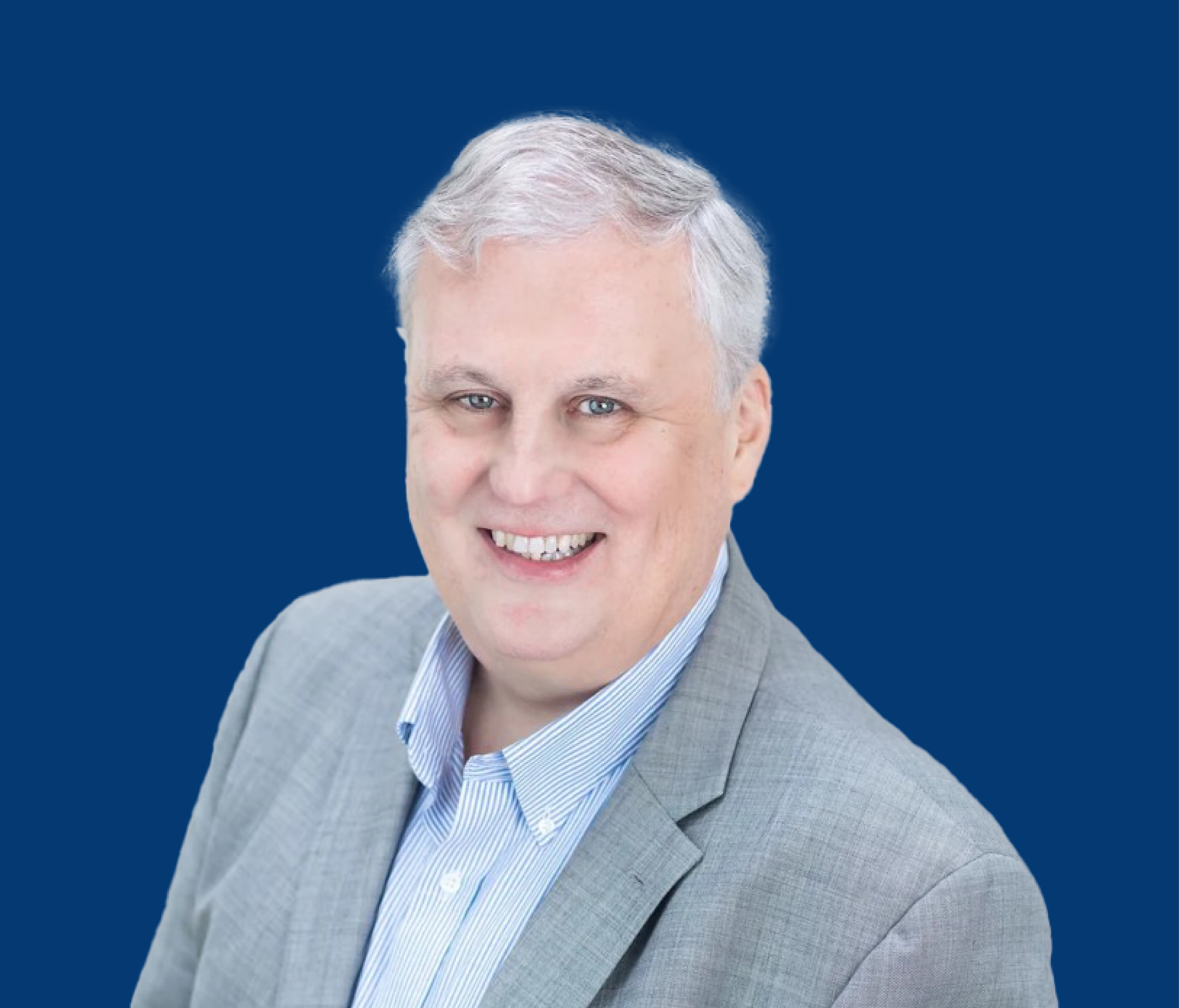 Professional headshot of a smiling middle-aged man with gray hair, wearing a light gray suit and blue striped shirt, against a solid dark blue background.