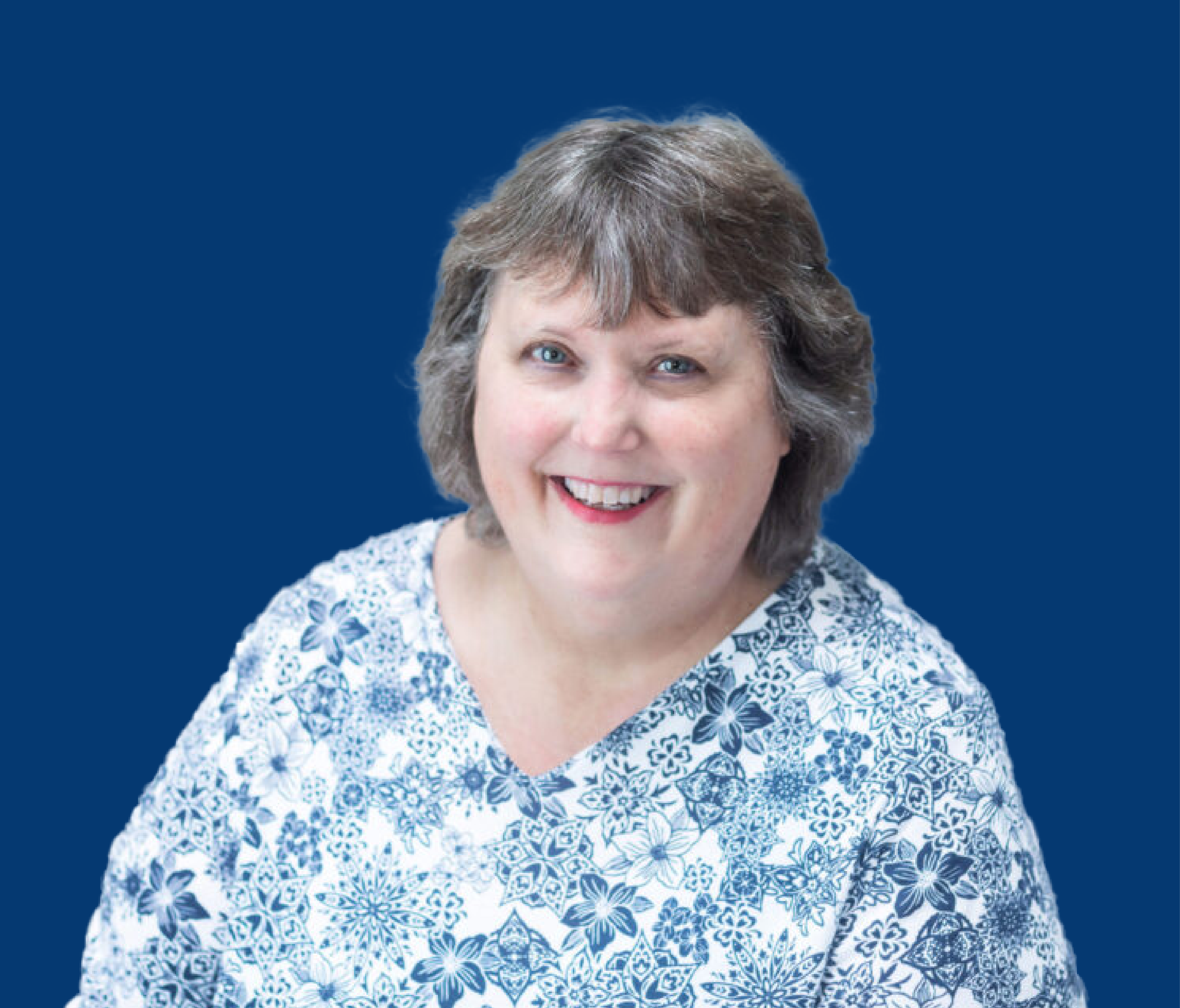 A woman with gray hair and blue eyes smiling, wearing a blue and white floral patterned shirt, against a solid blue background.