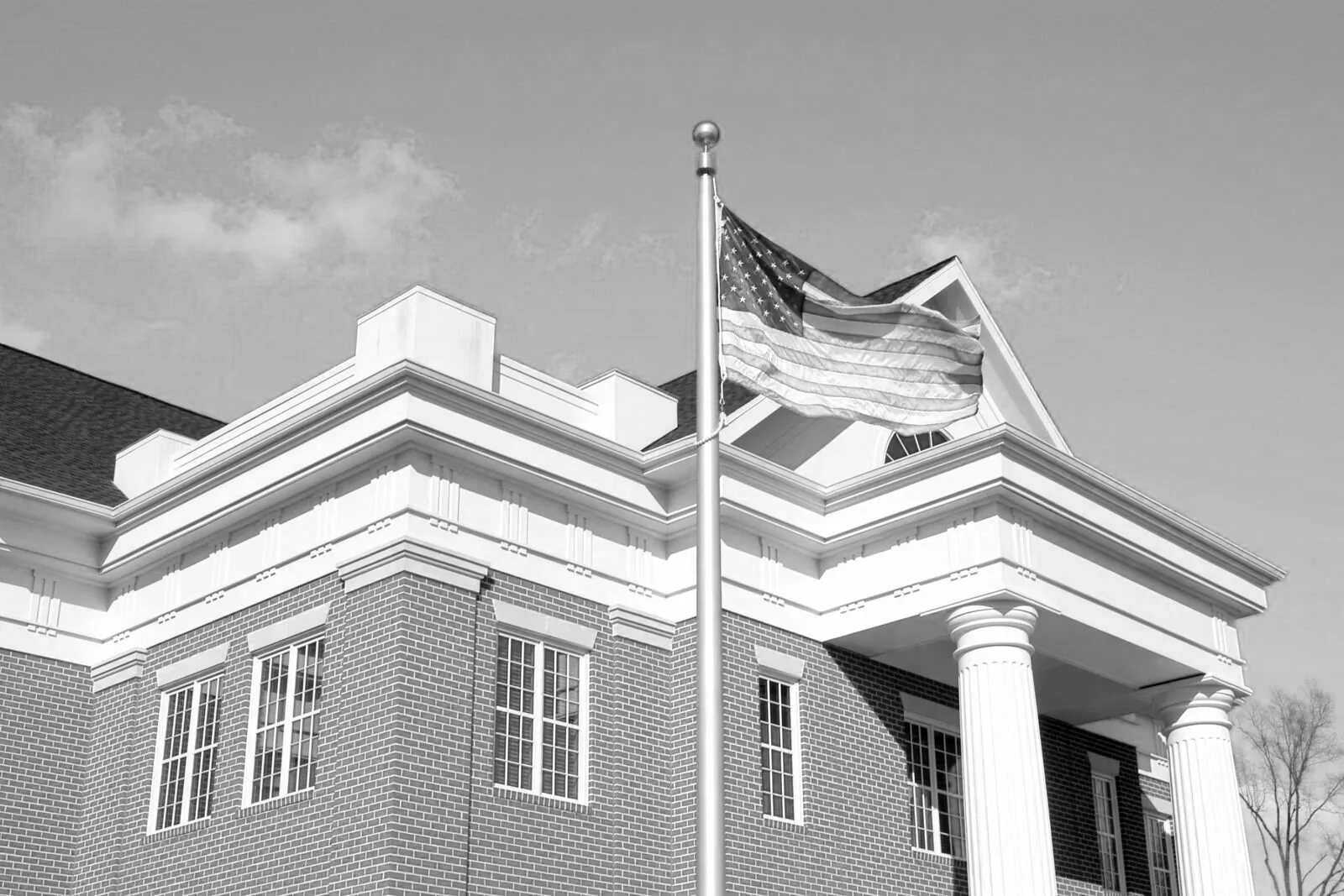 An American flag flying outside a brick building with white columns and decorative trim.