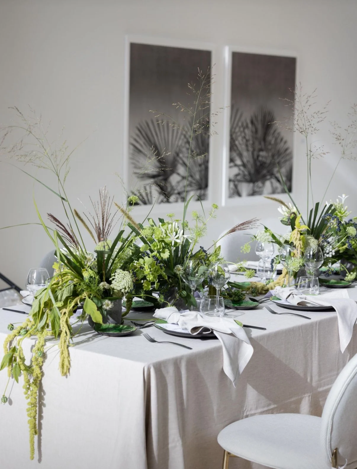 A banquet table decorated with lush floral arrangements, wine glasses, and white napkins, set against a neutral-colored wall with two abstract black and white framed artworks.
