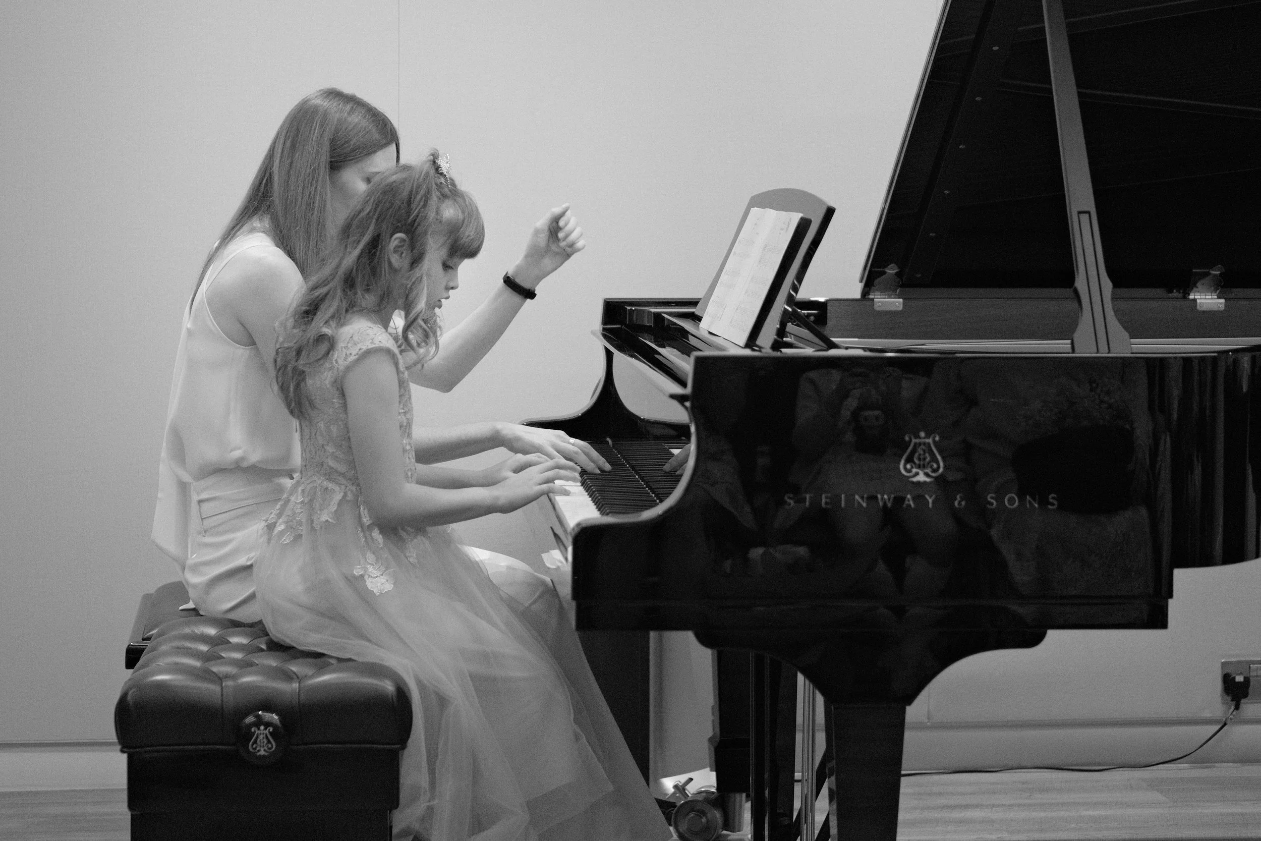 A woman and a young girl playing piano together in a music room.