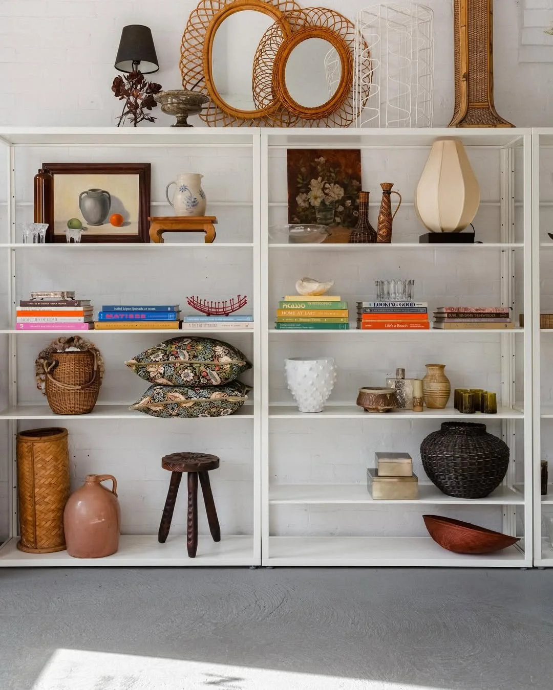 White bookshelf filled with decorative items, books, vases, mirrors, and art pieces, set against a white brick wall.