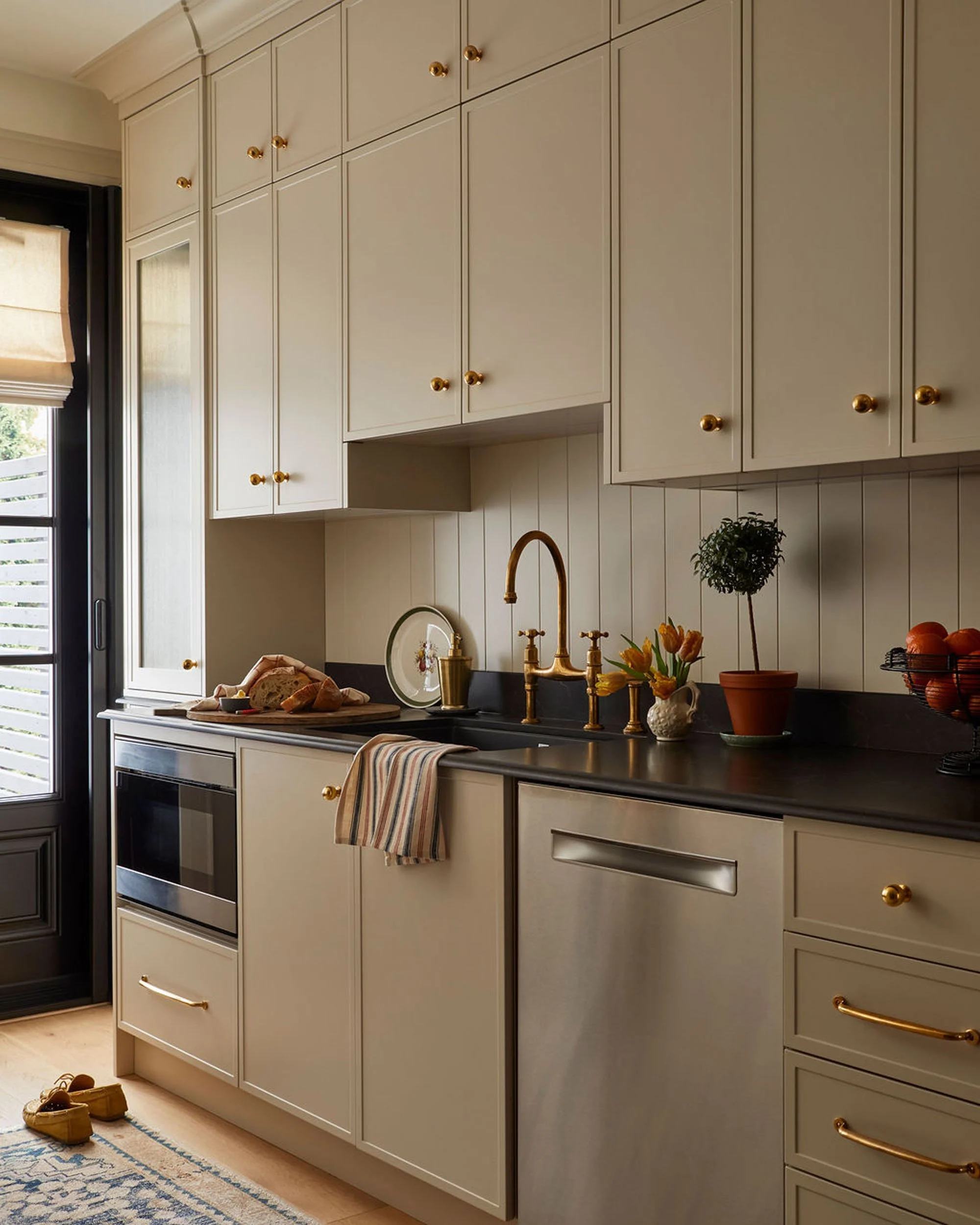 Kitchen with white cabinets, black countertop, gold fixtures, potted plant, and some baked bread on a cutting board.