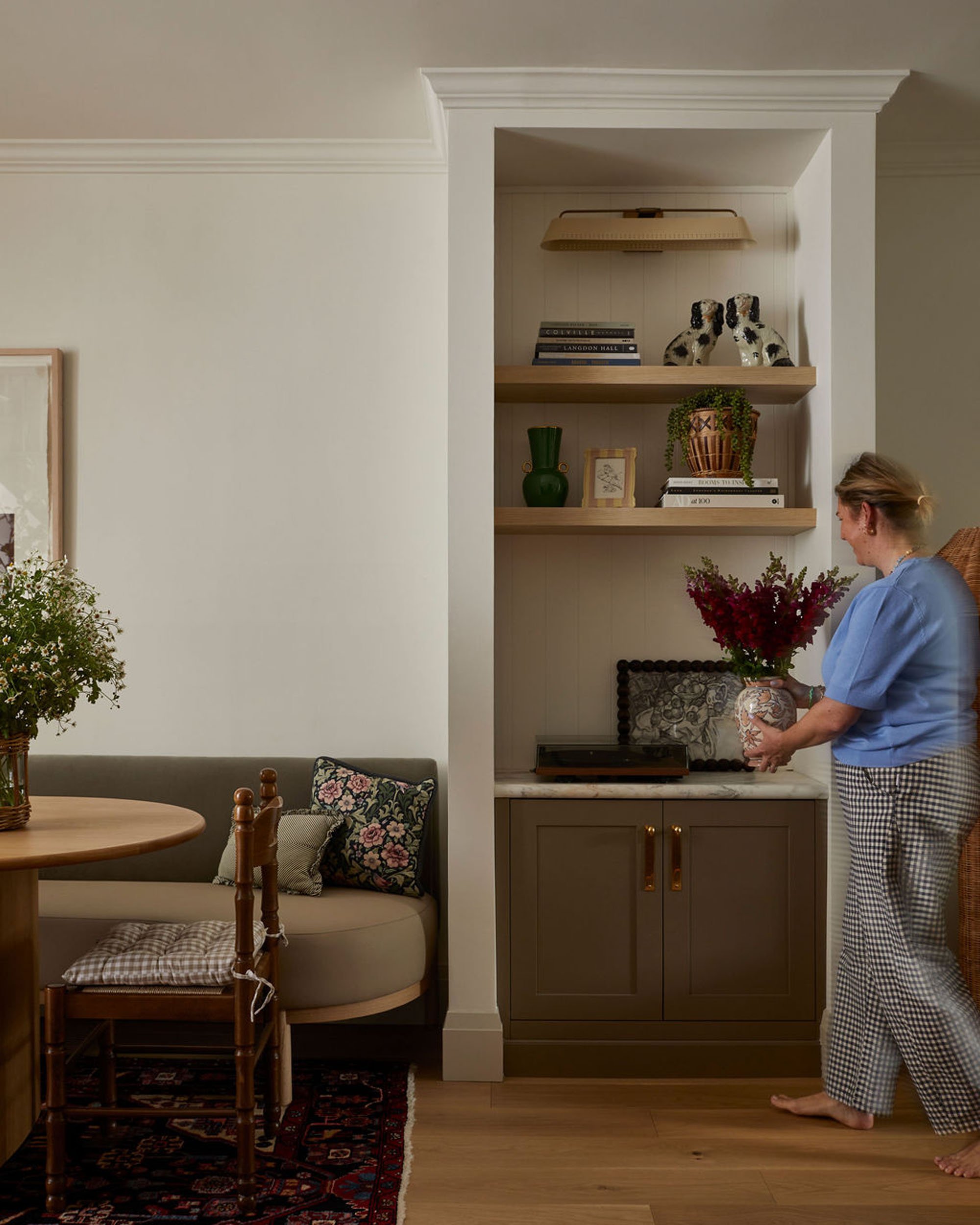 Woman placing a flower arrangement in a decorative vase on a cabinet in a cozy living room.