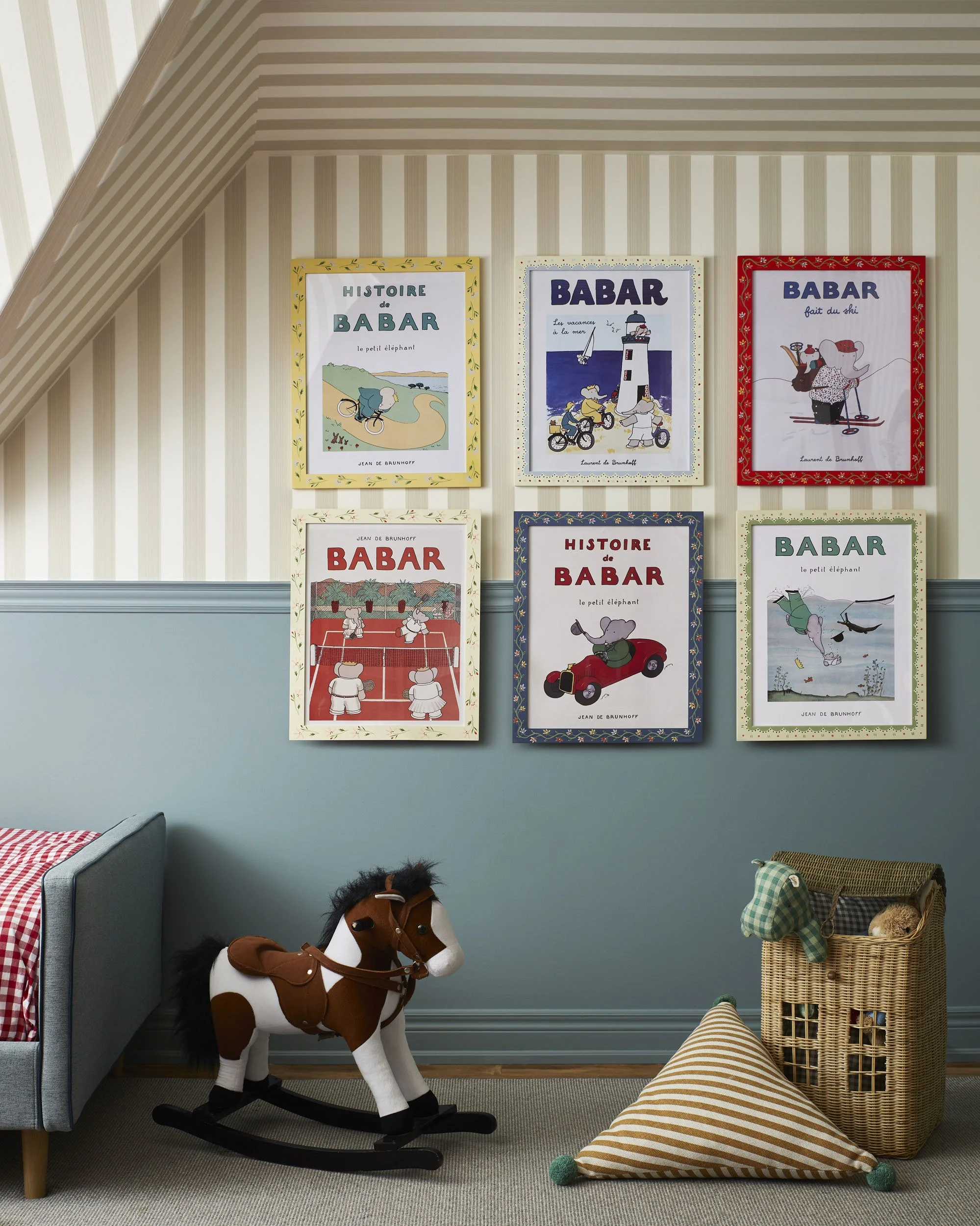Child's nursery with vintage-style 'Babar' picture frames on the wall, a rocking horse toy, a wicker basket, and a striped pillow on the floor.