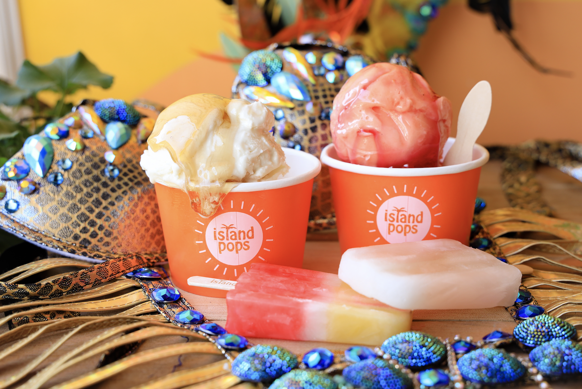 Carnival tabanca flavors: Two cups of ice cream, one with vanilla and caramel, the other with pink ice cream, on a decorative tropical-themed table with bright colors and shiny embellishments.