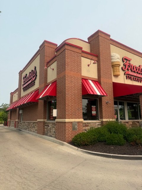 Awnings installed at Freddy's restaurant with red and white striped awnings, large sign with a beer mug and ice cream cone, and the name 'Freddy's.'