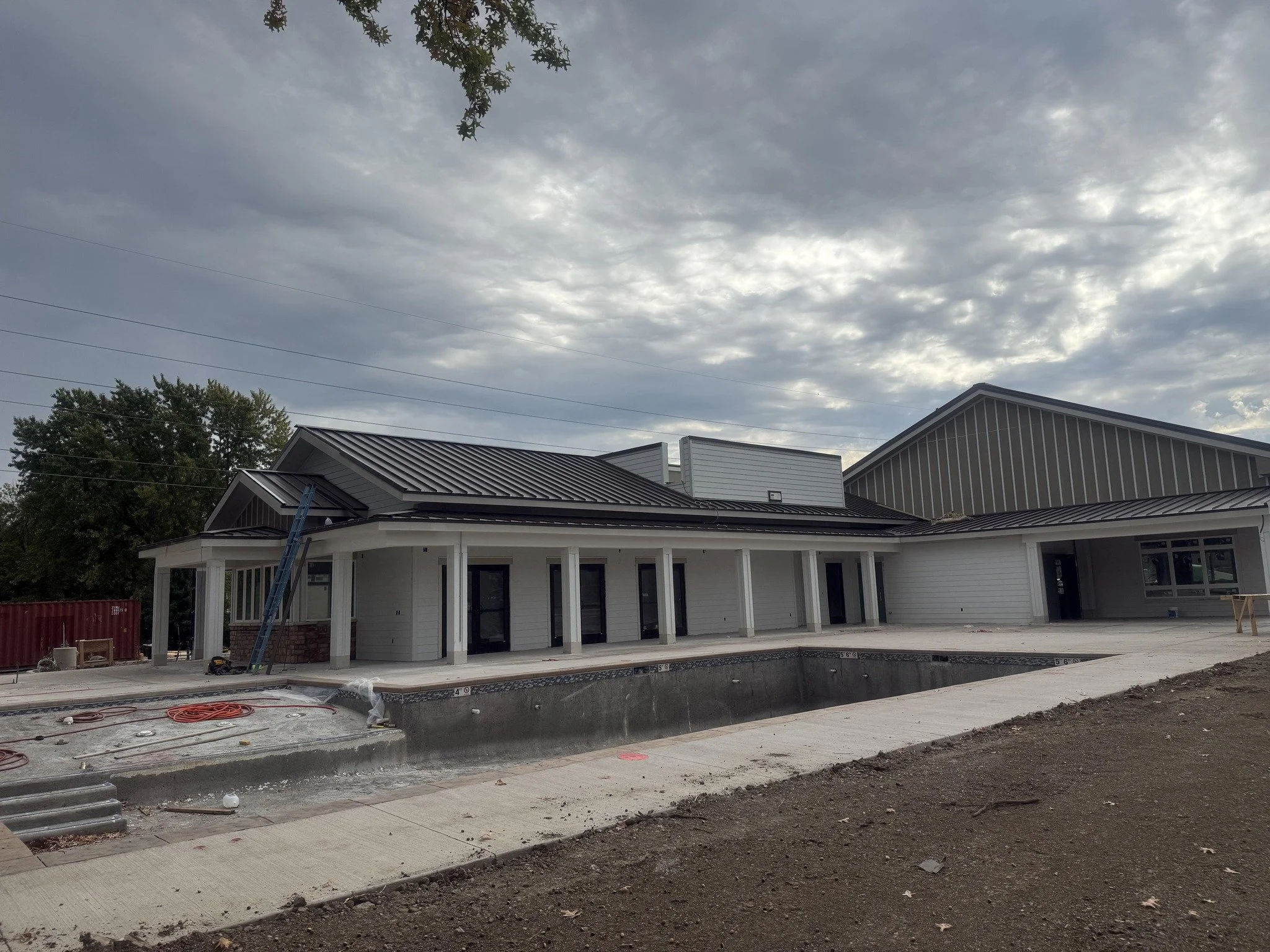 Under construction house with a swimming pool under a cloudy sky during daytime. Standing seam roof.