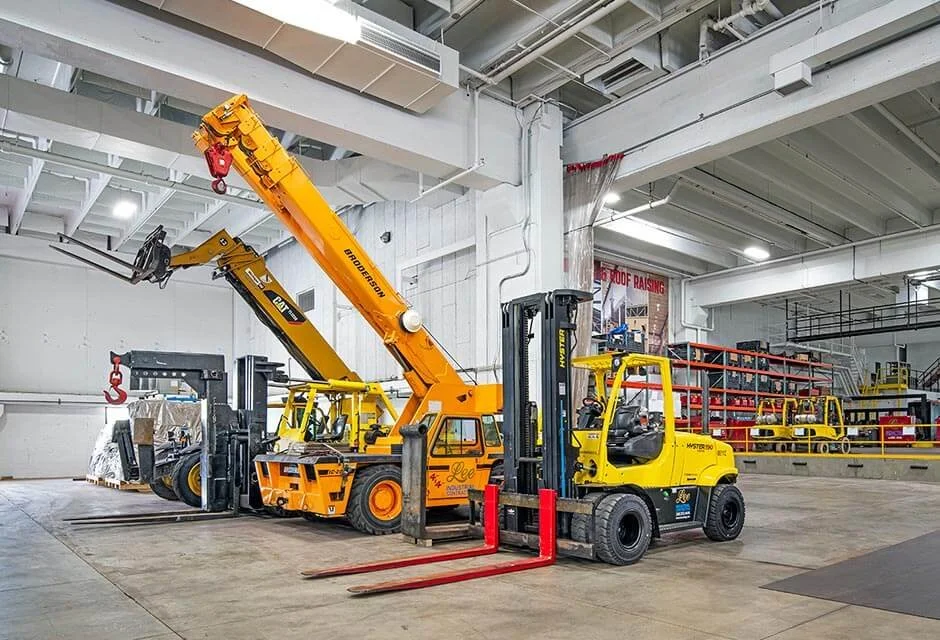 Industrial warehouse with yellow forklifts and a large orange crane lifting items. Red safety barriers and shelving units are visible in the background.