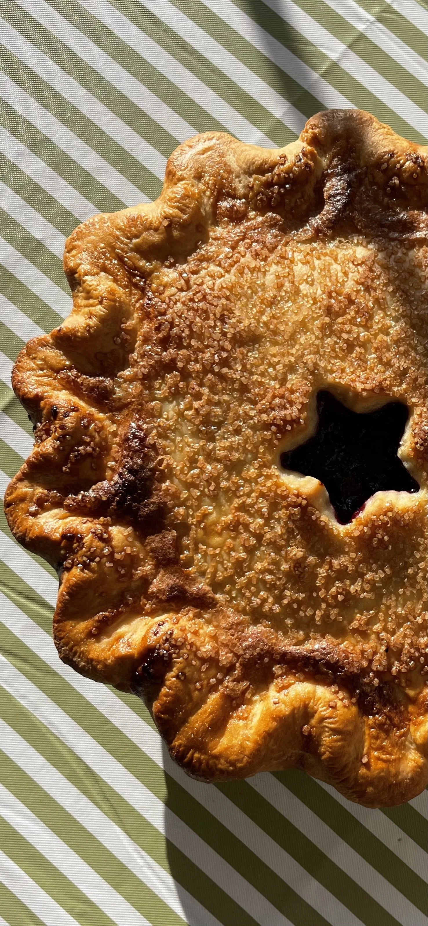 A star-shaped pastry with a golden-brown crust topped with sugar crystals, placed on a green and white striped surface.