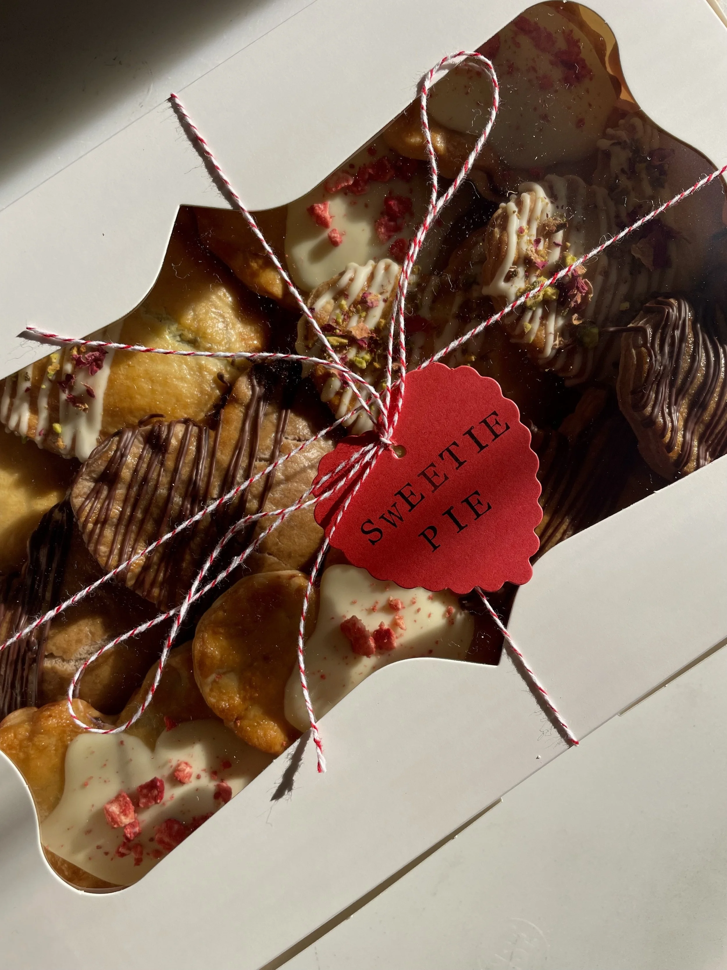 Box of assorted sweet pastries with a red heart-shaped tag that says 'Sweetie Pie', tied with red and white string.