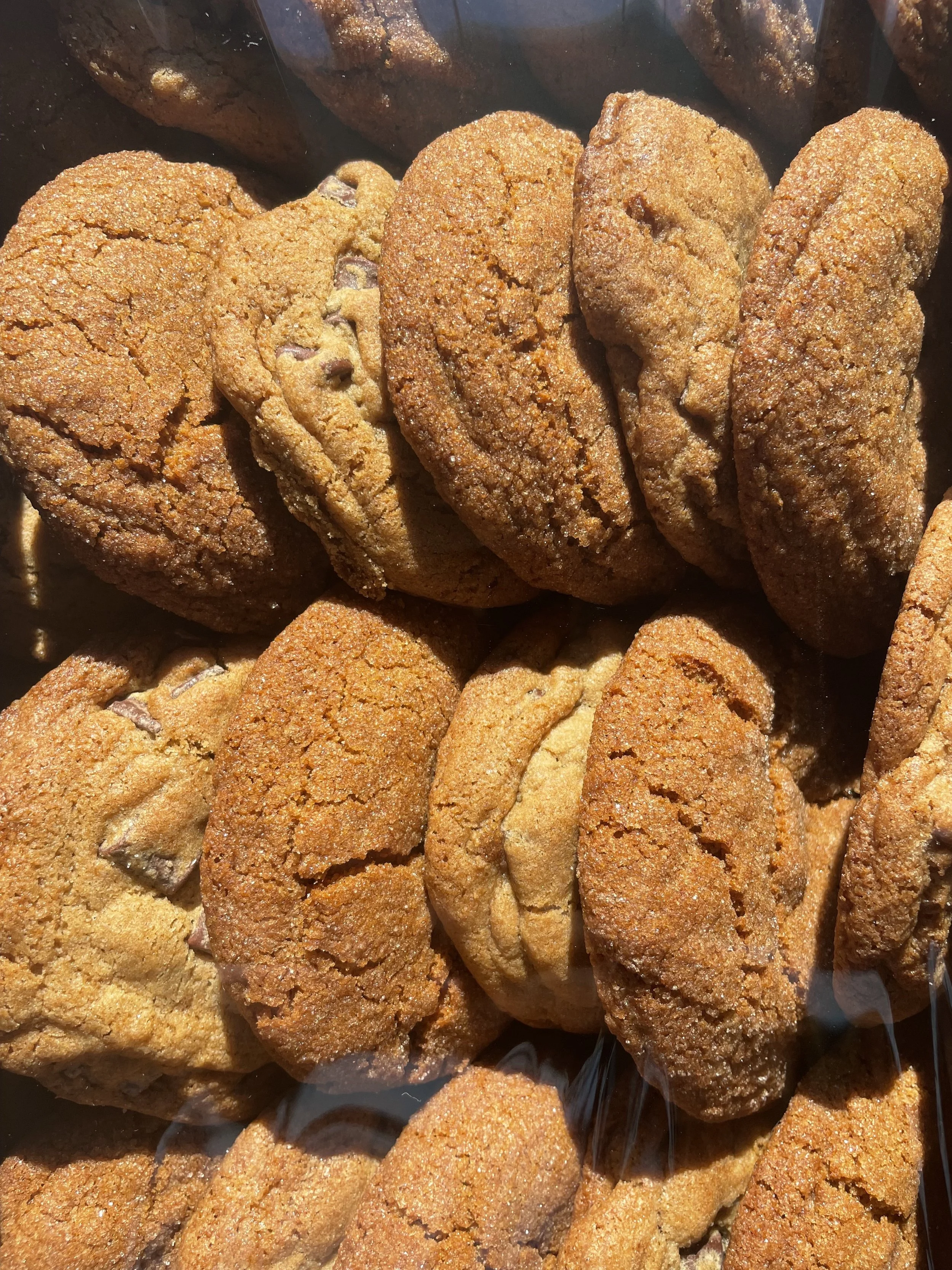 A close-up of several chocolate chip cookies with a golden-brown crust, some with visible chocolate chips, arranged in a tray.