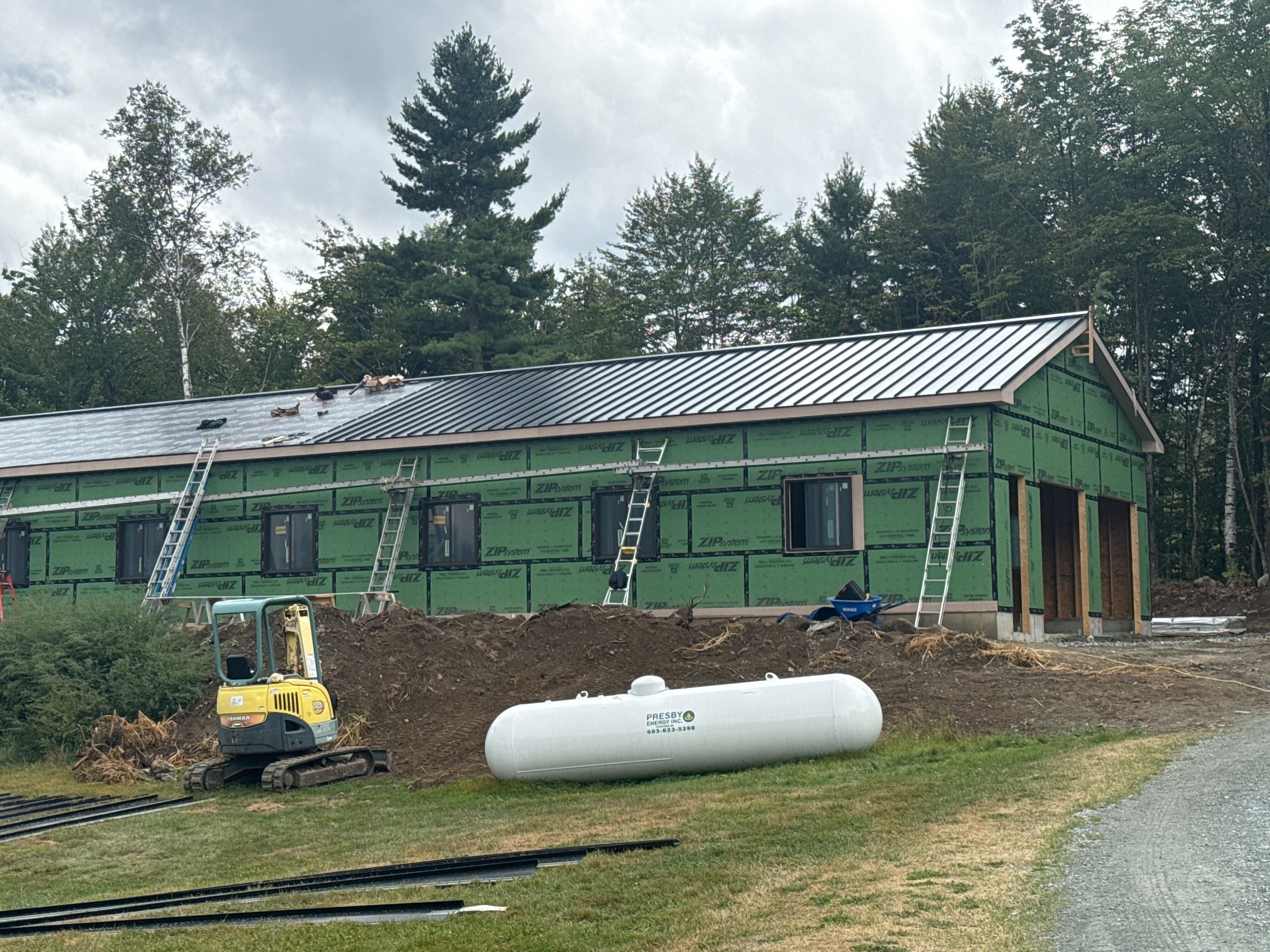 Construction site of a residential building with green sheathing, windows, and a metal roof, surrounded by construction tools and equipment.