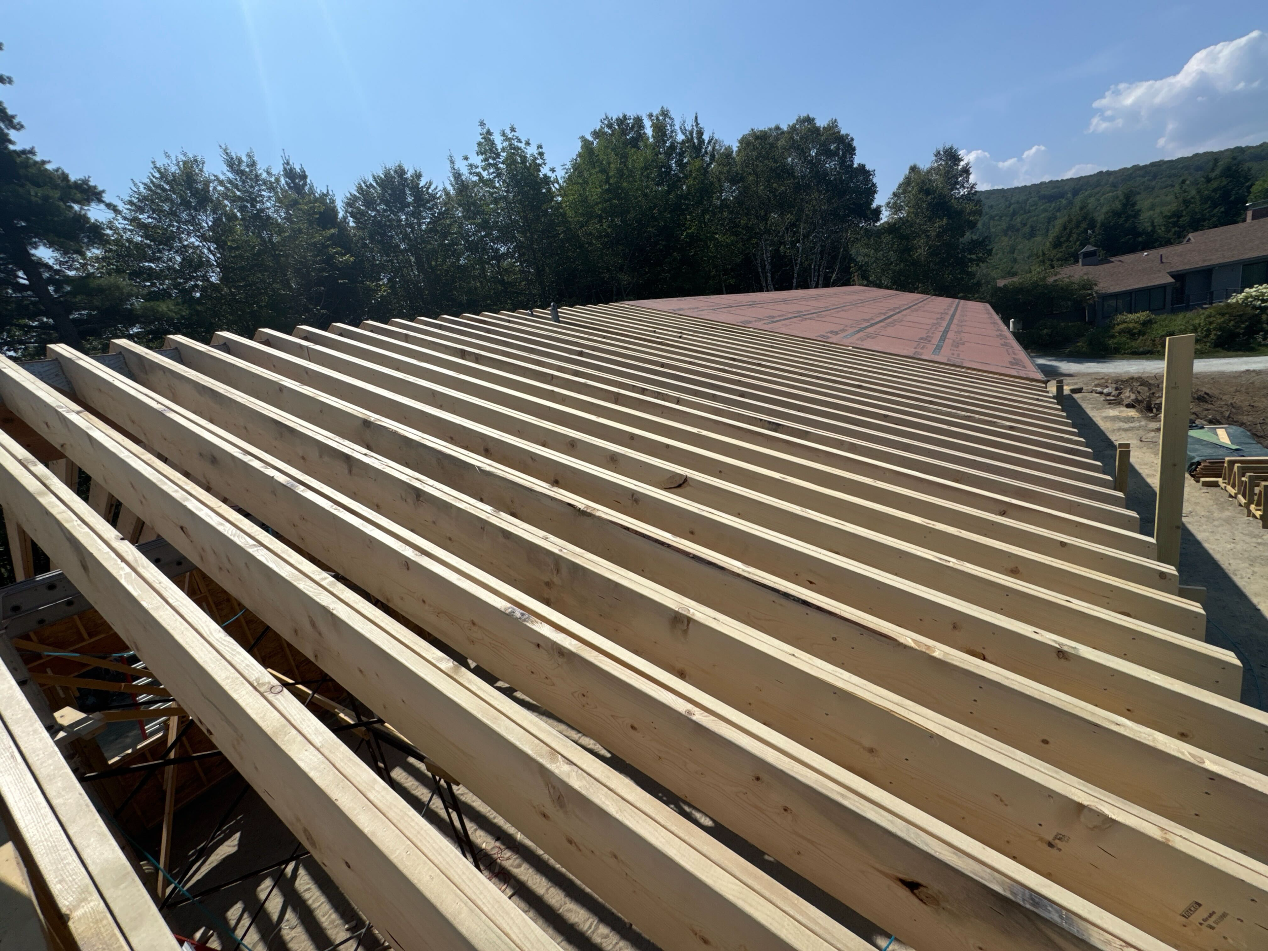 Construction site with wooden roof framing in progress, with exposed roof rafters and mountains in the background.