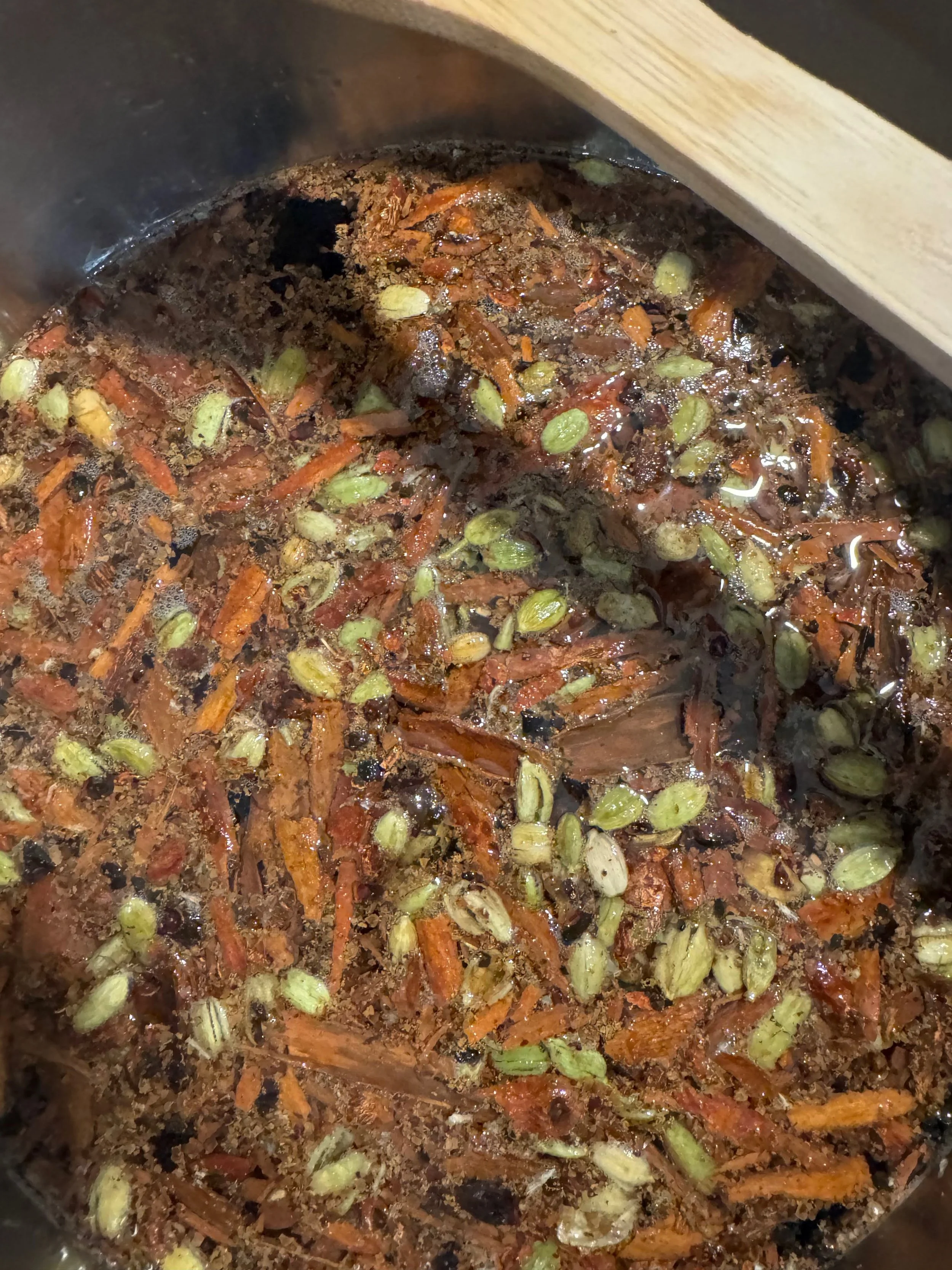 Mezcla gourmet de especias para Masala Chai con vainas de cardamomo verde, rajas de canela y té negro infusionando en olla de acero.