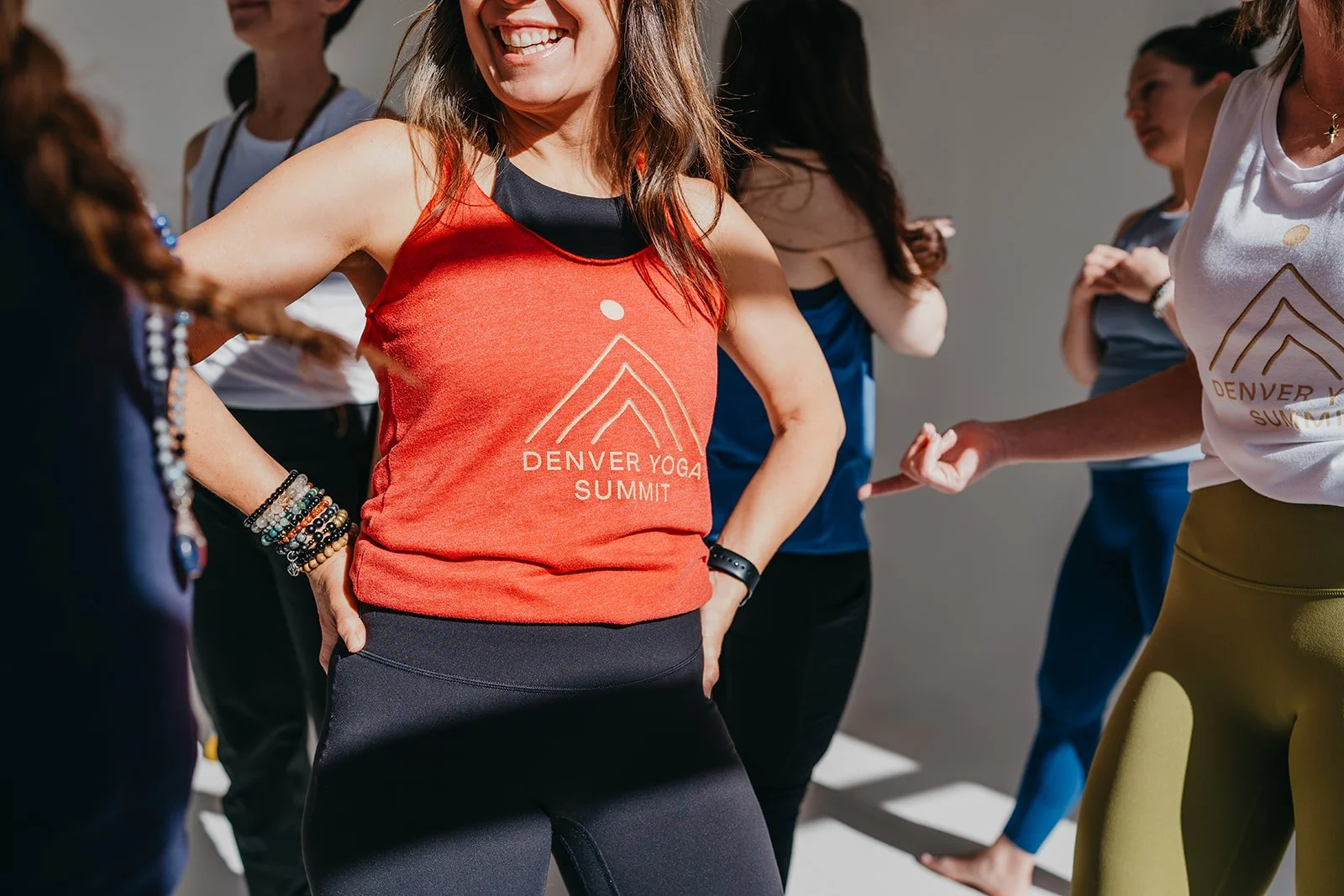 Smiling woman in red Denver Yoga Summit tank top in a community gathering in the sunshine.