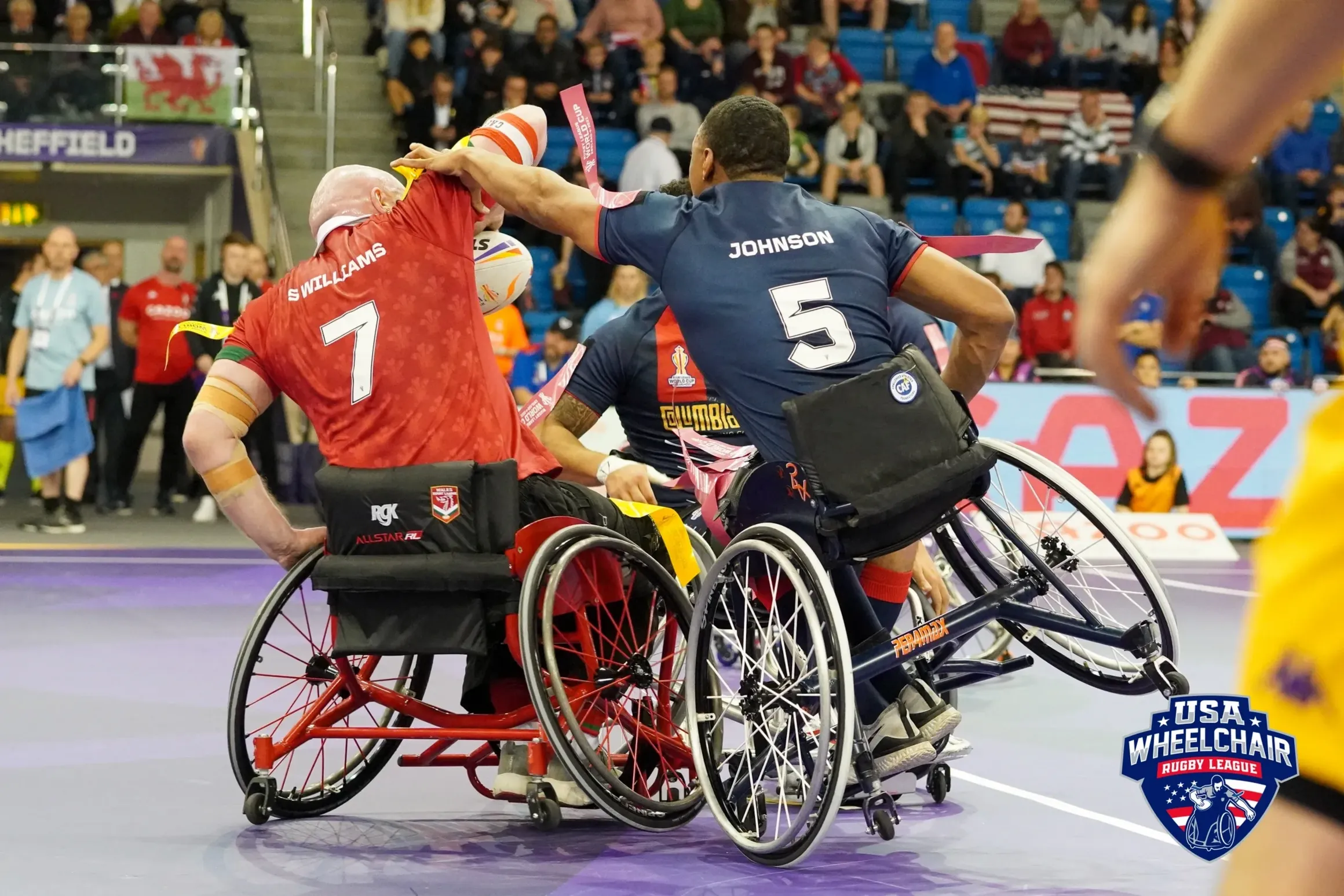 Two wheelchair rugby players in action during a game at the USA Wheelchair Rugby League, with spectators watching in the background.