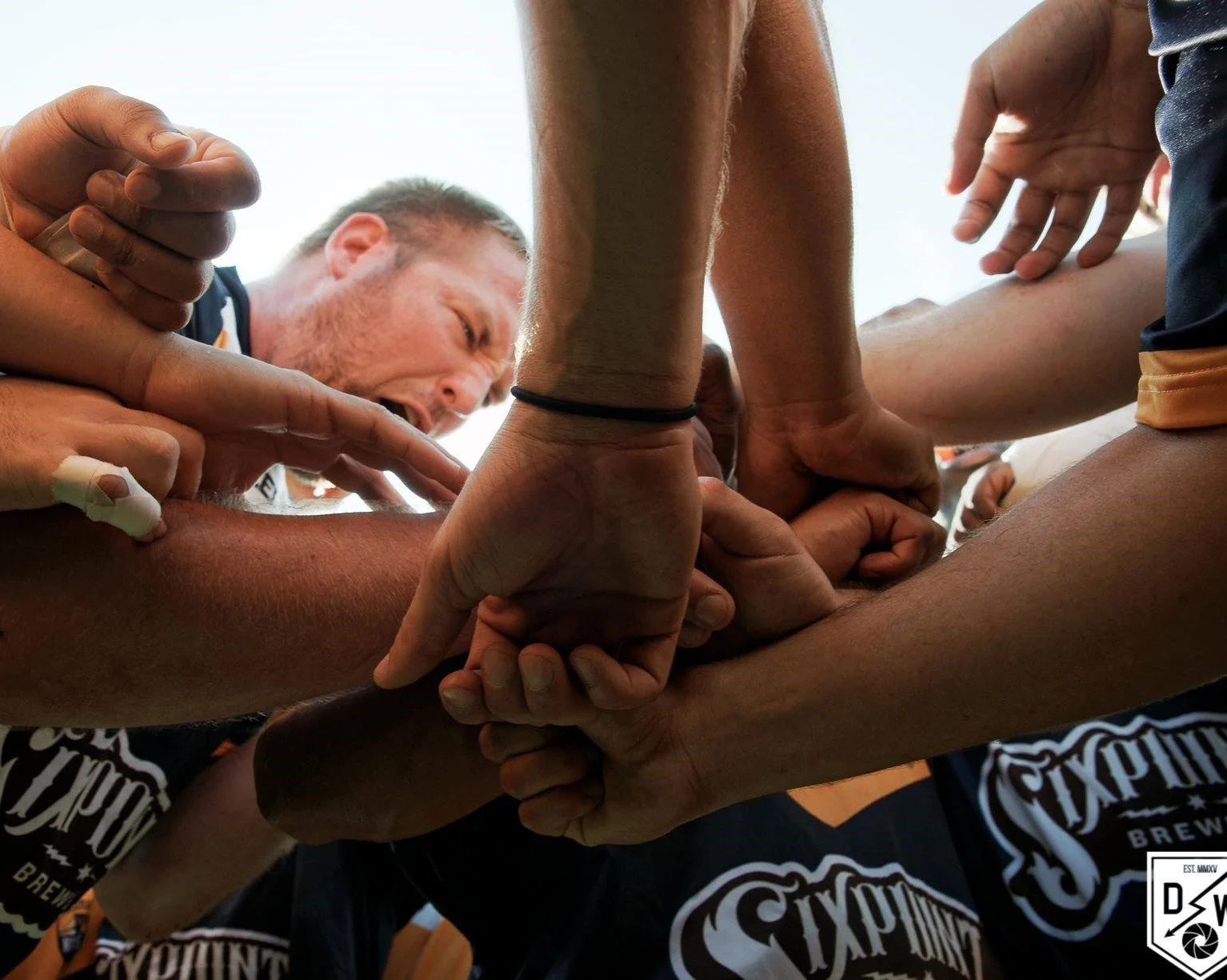 A group of people in a sports huddle, holding hands together in the center.