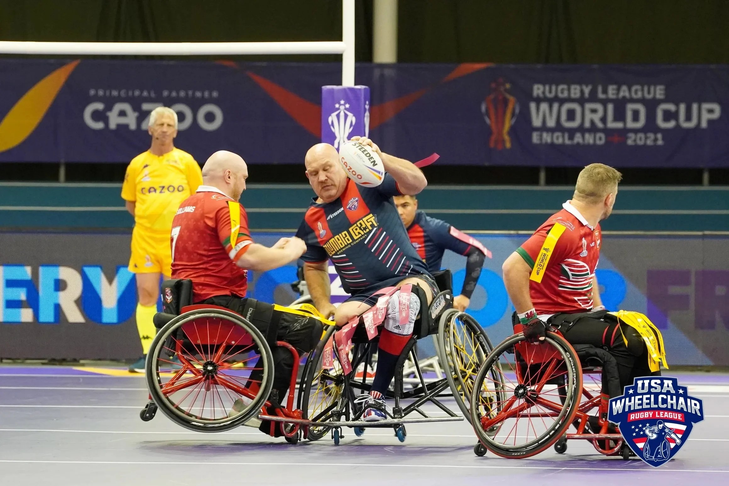 Wheelchair rugby players in action during the 2021 Rugby League World Cup in England, with one player holding a ball and others on the court.