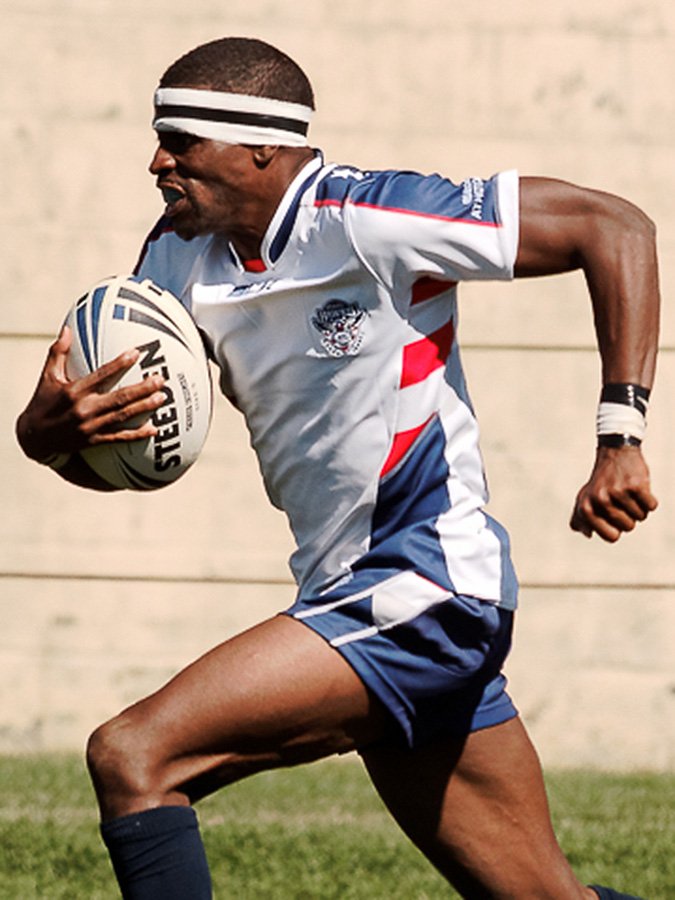 A man in a rugby uniform running while holding a rugby ball.