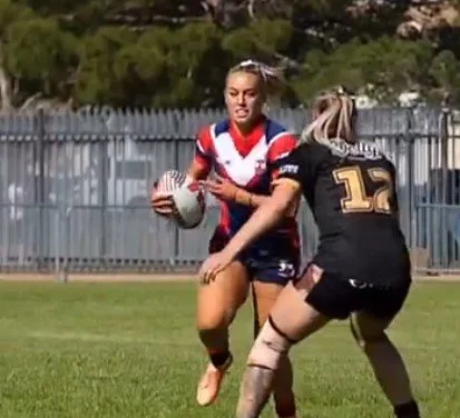 Rugby player in red and blue uniform holding a rugby ball while running on the field, tackled by an opponent wearing a black uniform with a number 12 jersey.