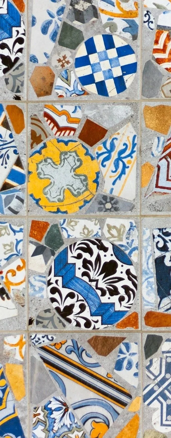 Close-up of a colorful mosaic made of various decorative ceramic tiles, featuring geometric patterns and floral designs in shades of blue, yellow, orange, black, gray, and white.