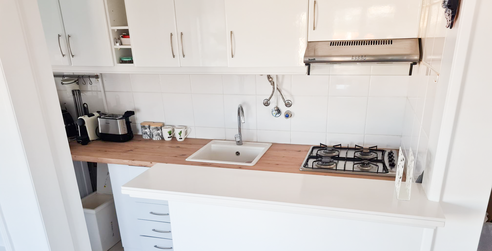 Kitchen with white cabinets, a wooden countertop, a small sink, a gas stove, and various small appliances like a toaster and a kettle.
