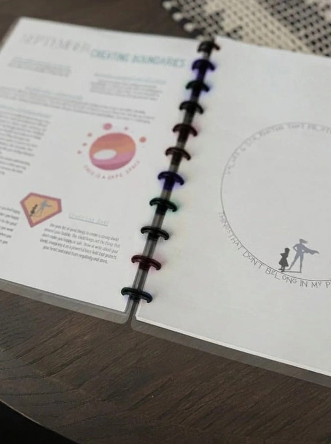 An open planner with colorful rings lies on a wooden table, displaying text and graphics about creating boundaries.