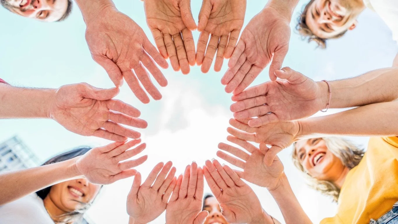 Ultimate Goal Book A diverse group of people holding their hands together in a circle, smiling and looking up at the sky.