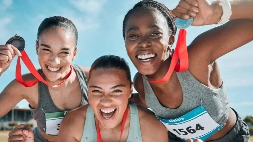 Ultimate Goal Book Three women at a race event celebrating with medals and race bibs, smiling and showing their medals.