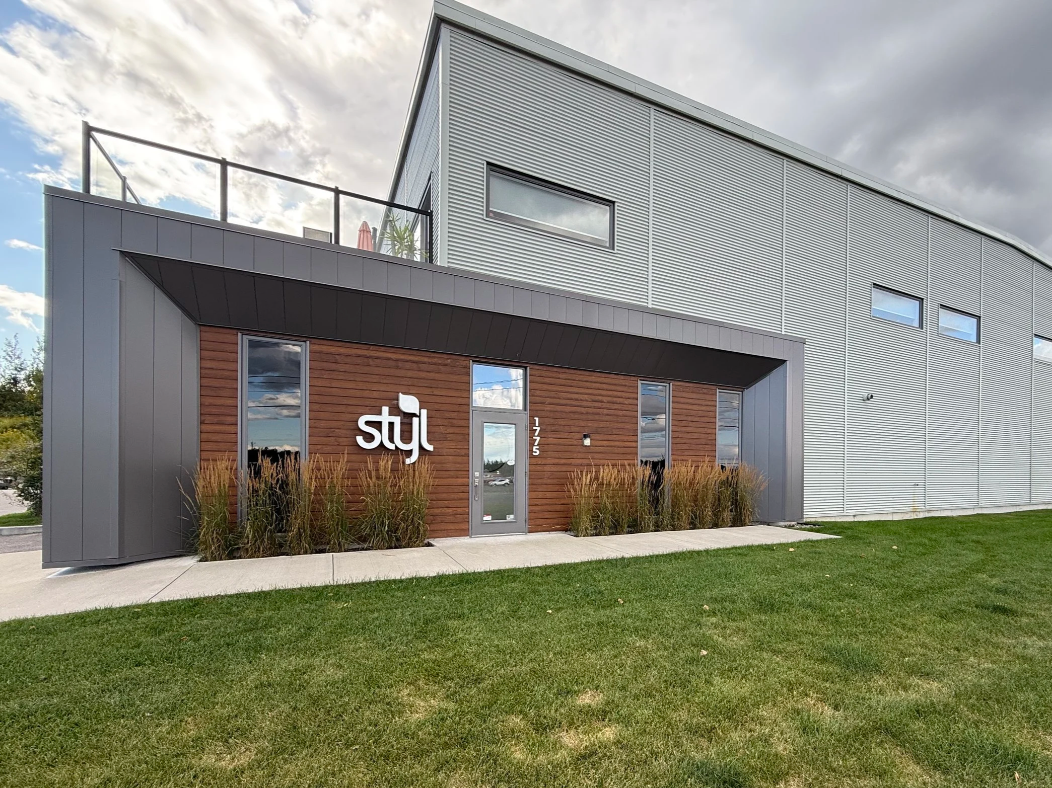 Modern commercial building with grey metal siding and wooden front facade, displaying the sign 'styl'.