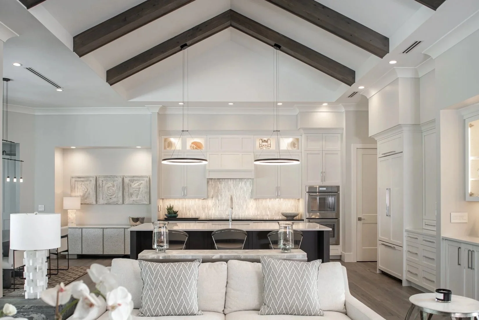 Modern kitchen with white cabinets, black island, and hanging circular pendant lights in an open-concept living space.