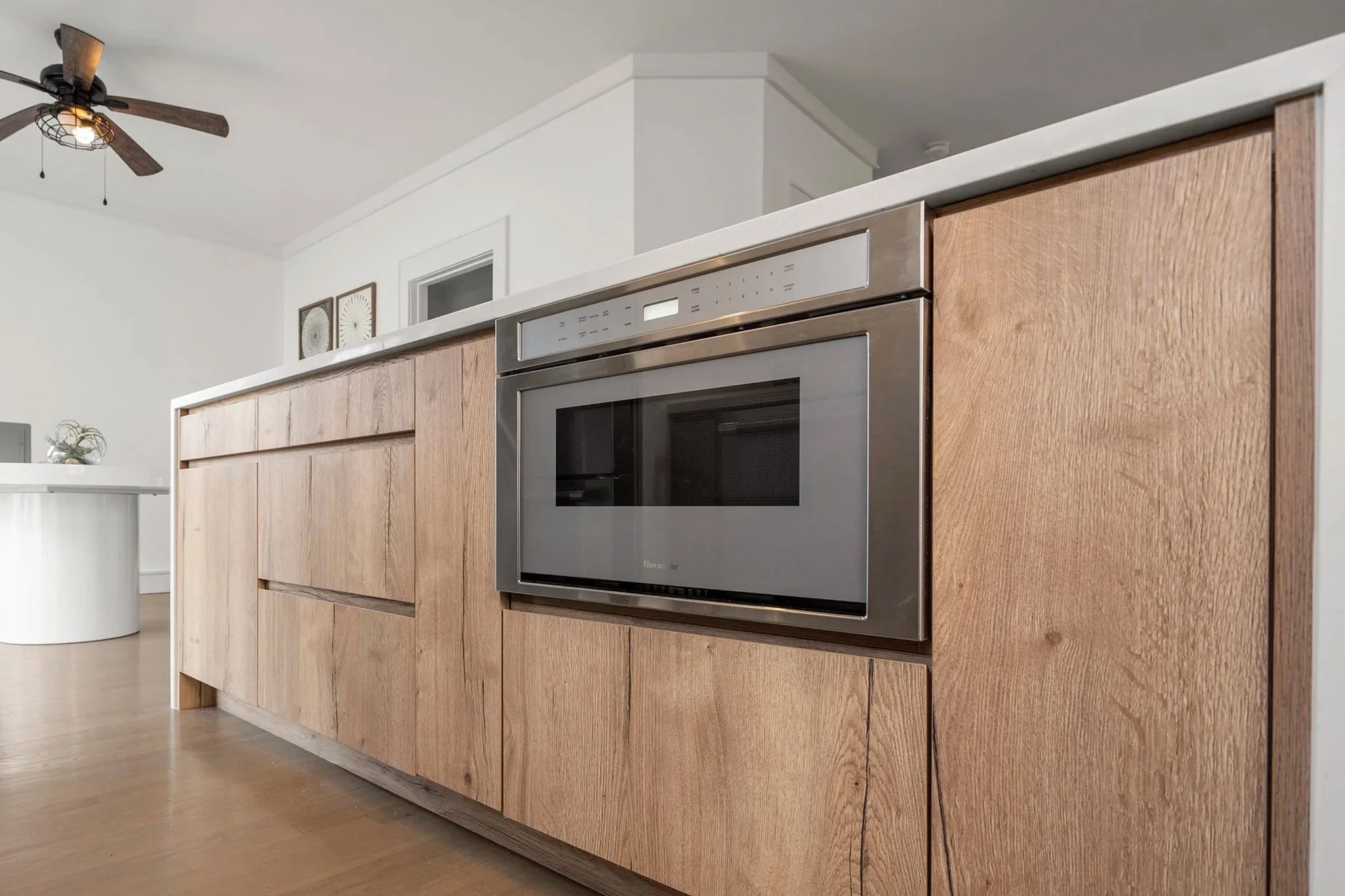 Close-up of a modern wooden kitchen cabinet with built-in stainless steel microwave and wooden flooring.
