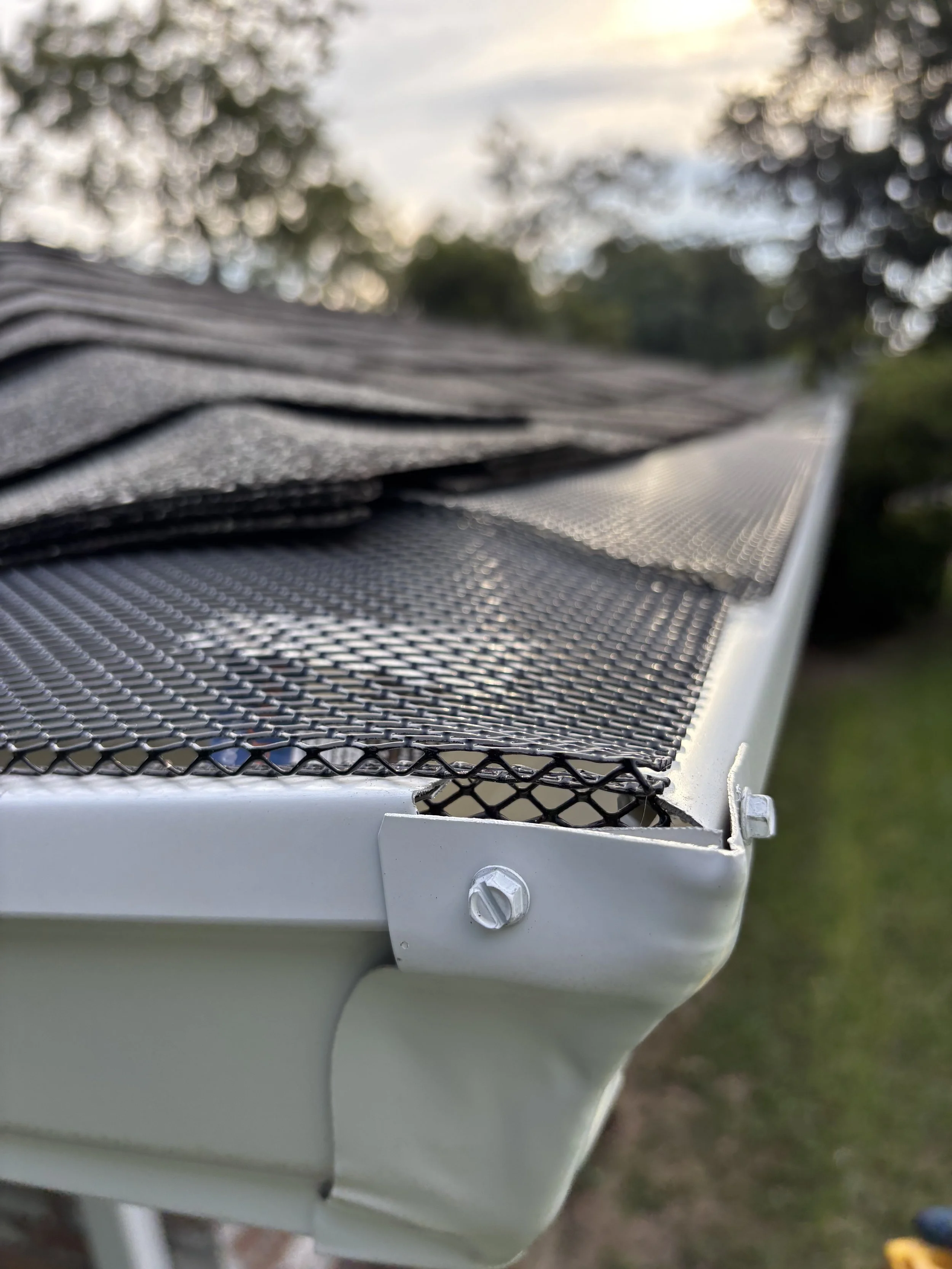 Close-up of a metal outdoor table with a mesh top, secured with screws, with a blurred background of trees and sky.