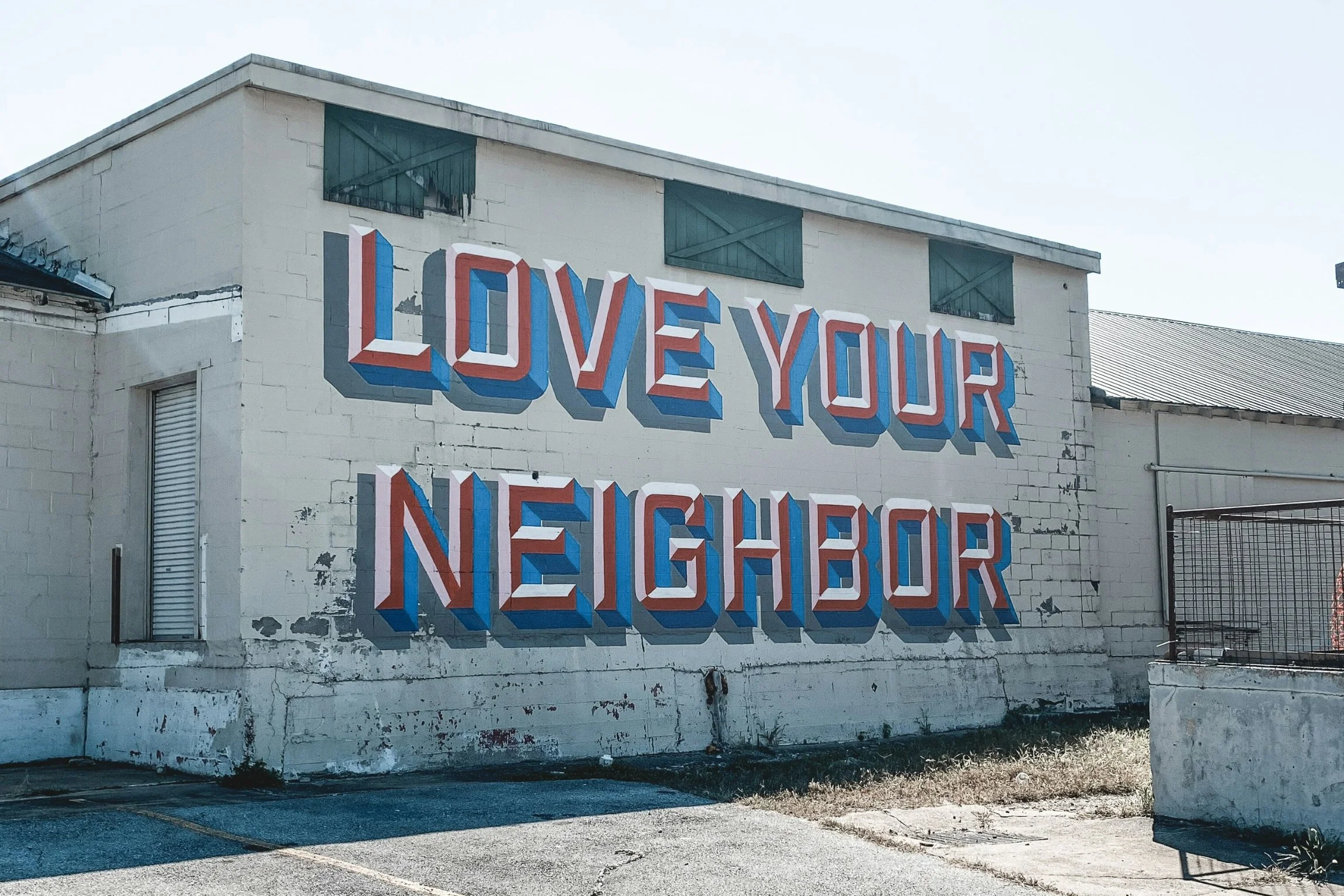 A large mural on the side of a building with the phrase 'Love Your Neighbor' in bold letters painted red, white, and blue.