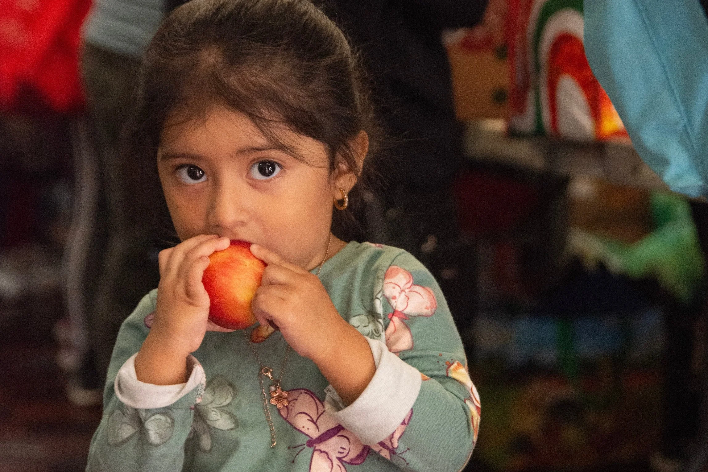 A young girl with brown hair and big eyes eating a red apple at Jericho Road Ministries location in Powderhorn neighborhood in Minneapolis, Minnesota.