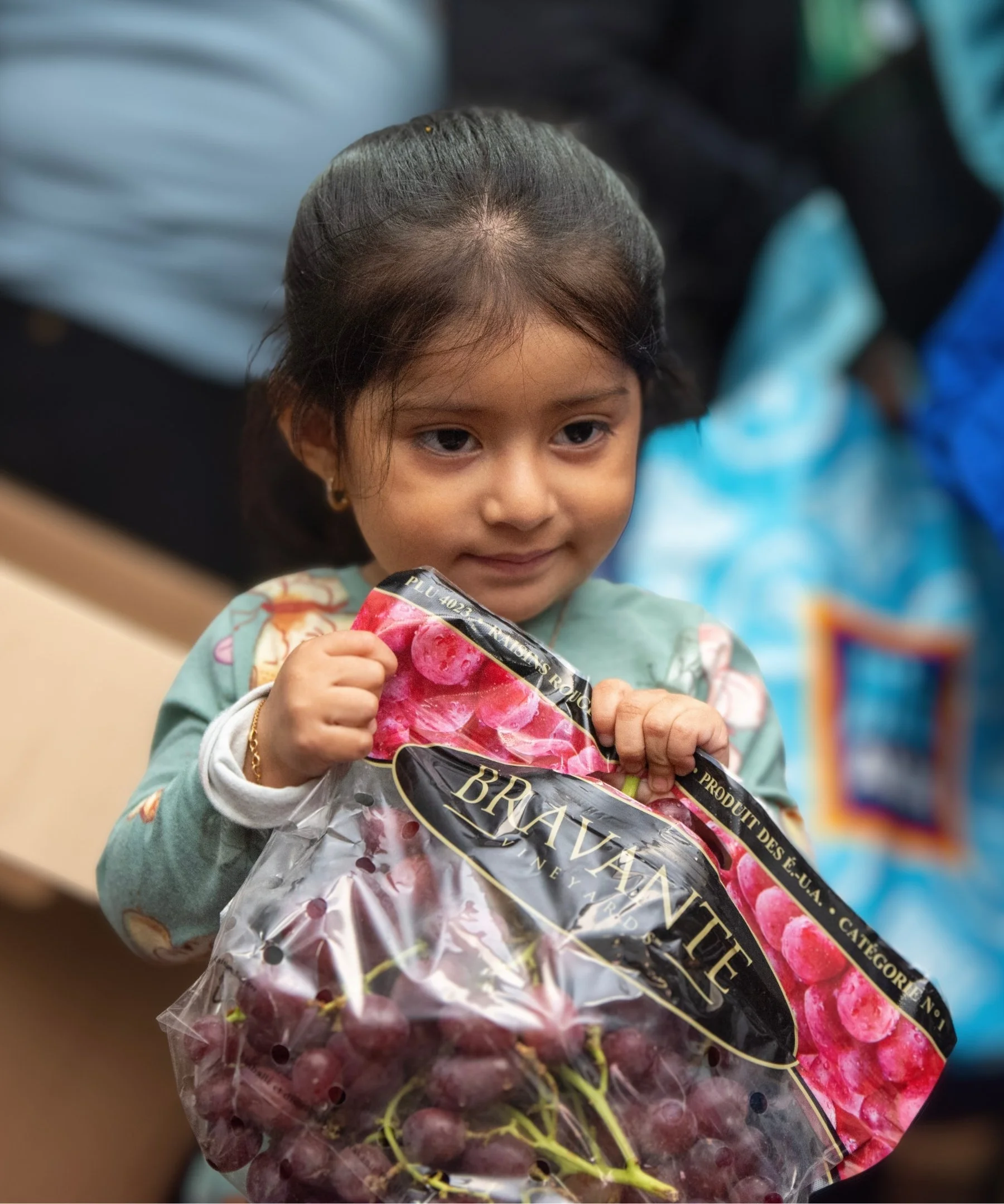 A young girl holding a bag of grapes with a slight smile at Jericho Road Ministries' food pantry in Minneapolis, Minnesota.