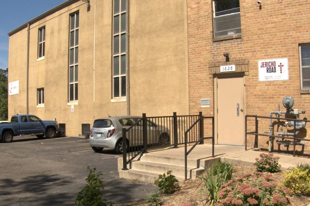 Exterior of a building with parking lot, parked cars, and a sign that reads 'Jericho Road.'